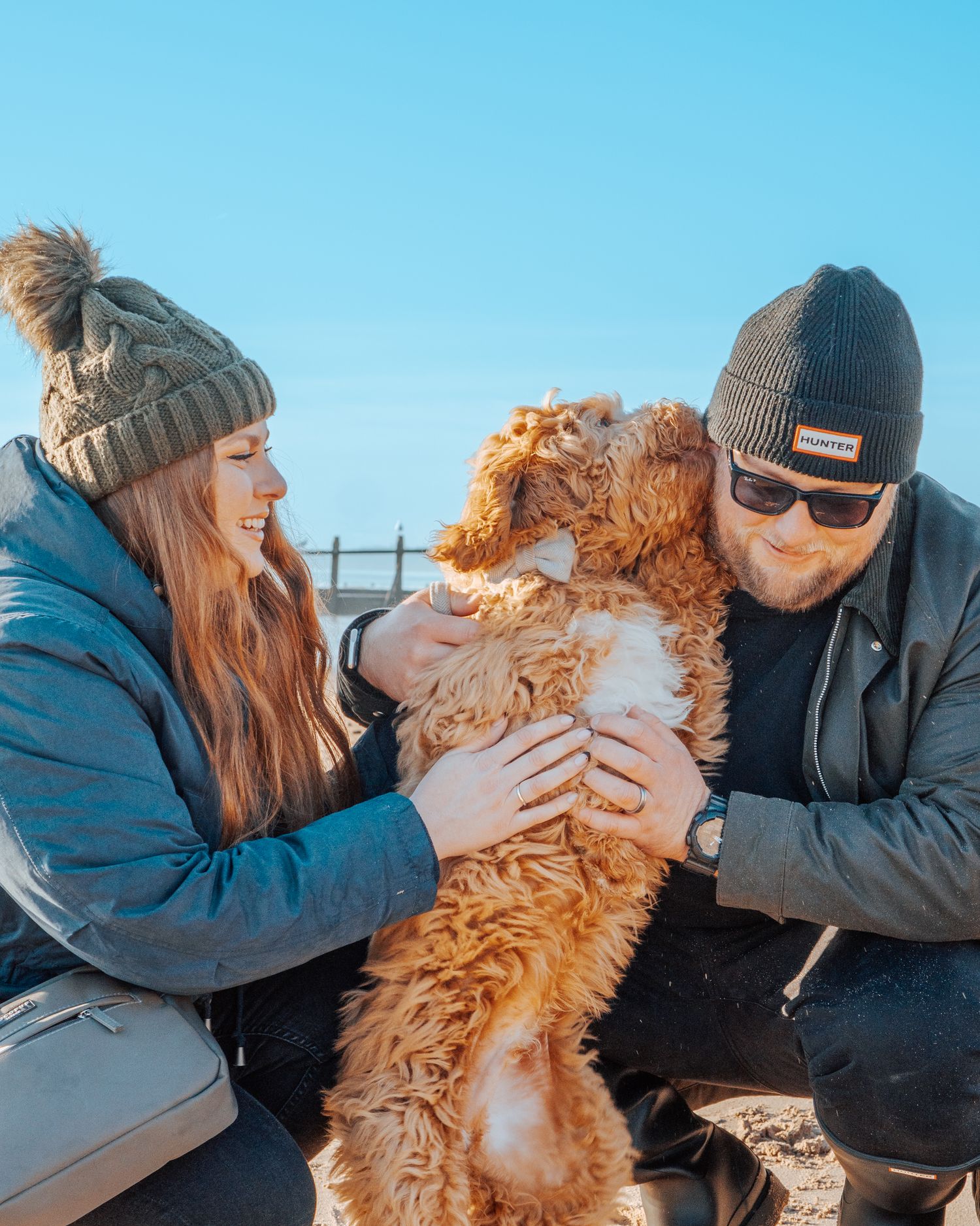 A couple shares tender moments with their fluffy golden doodle dog in a series of affectionate outdoor photos.