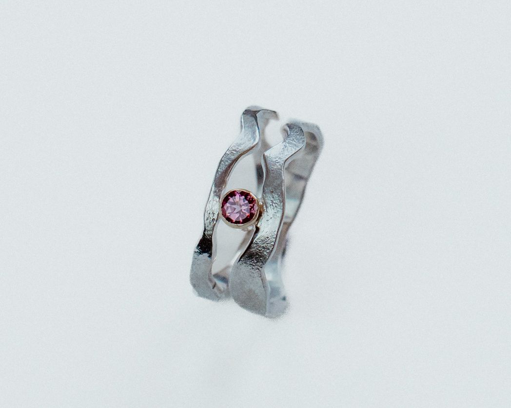 Close-up of a twisted silver ring with pink gemstone against white background.
