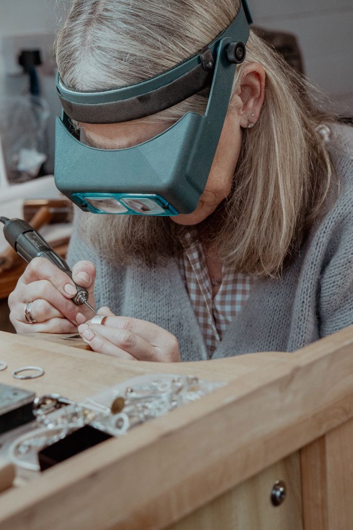 Close-up of hands working with jewellery tools while wearing magnifying headgear.