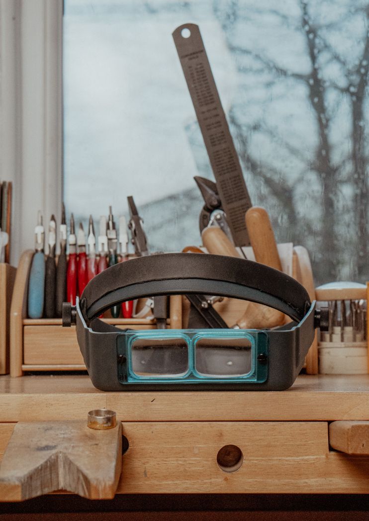 Jeweler's magnifying headband and tools arranged on wooden workspace.