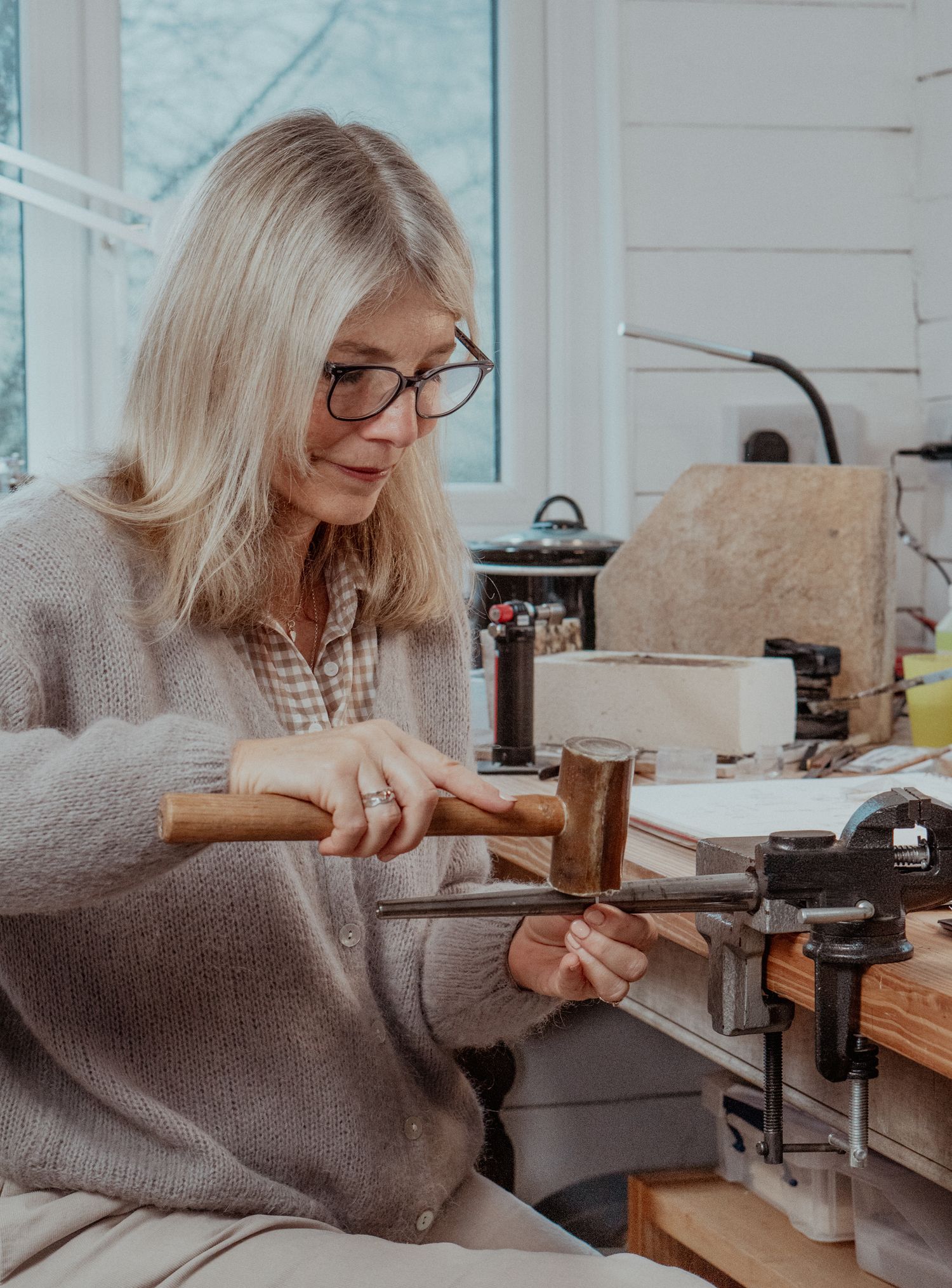 A person works at a jewelry crafting bench with tools and equipment.