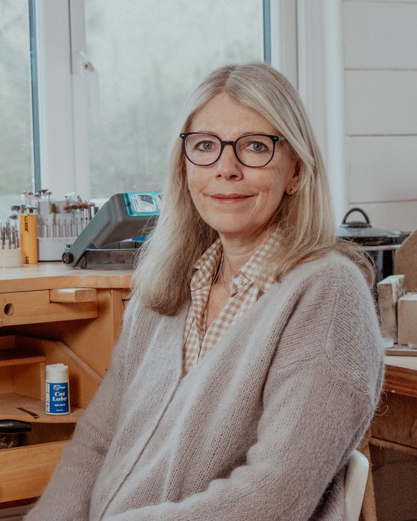 Artisan in cozy sweater sitting at creative workspace near window.