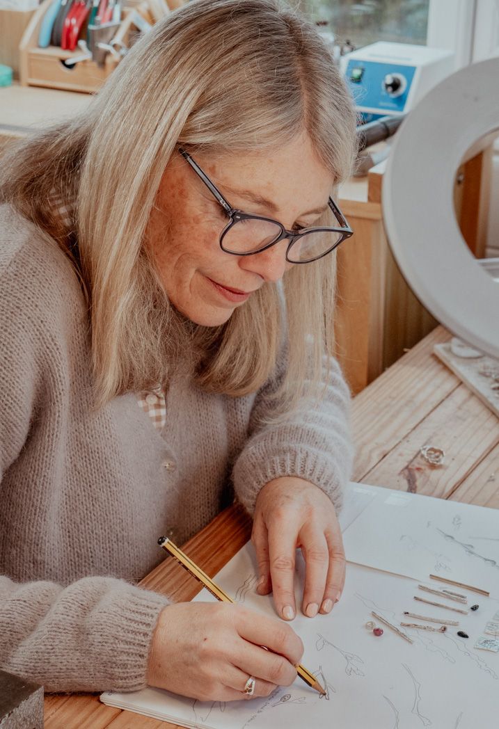 Artist carefully sketching or drawing at a wooden desk near a bright window.
