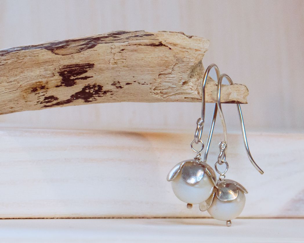 Silver drop earrings displayed against weathered driftwood on white surface.