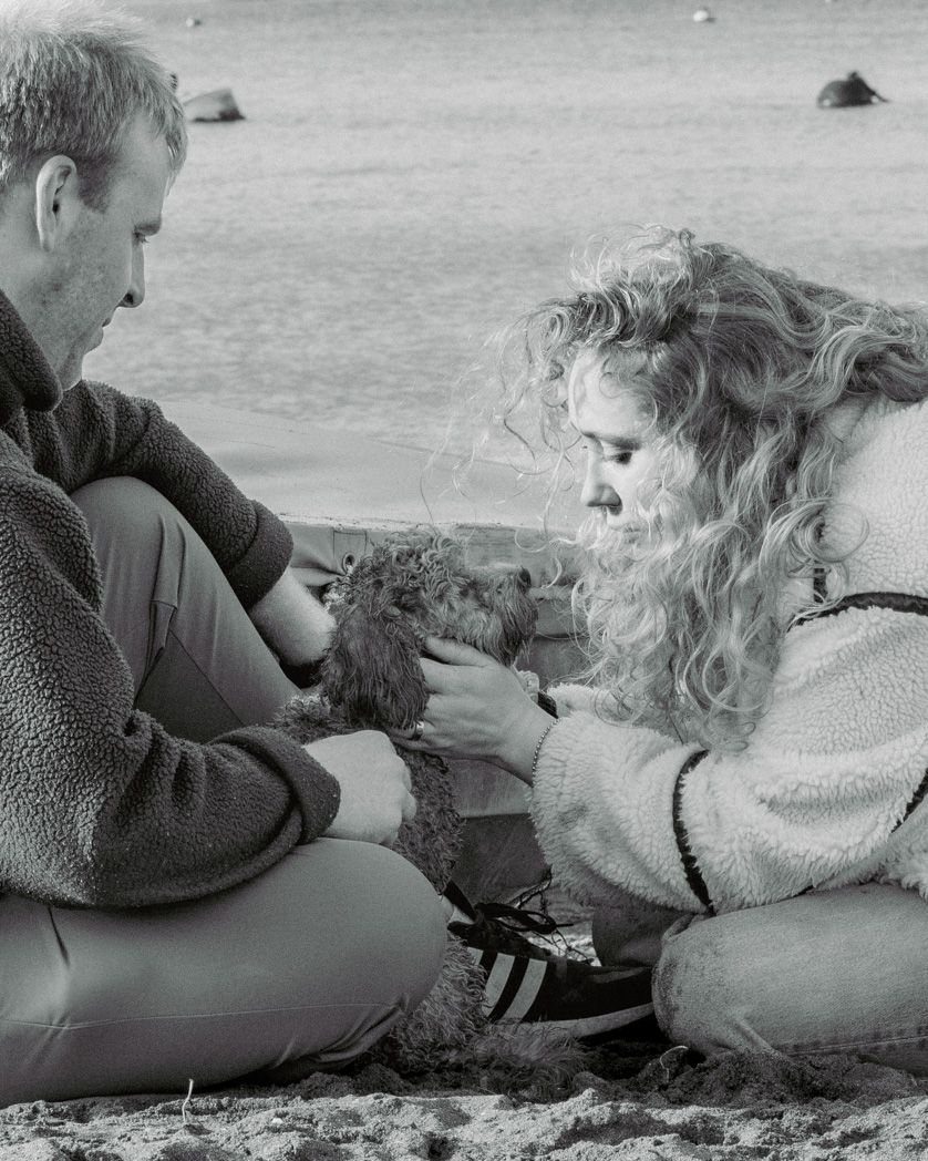 Two people examining something while sitting on beach sand in vintage black and white photo.