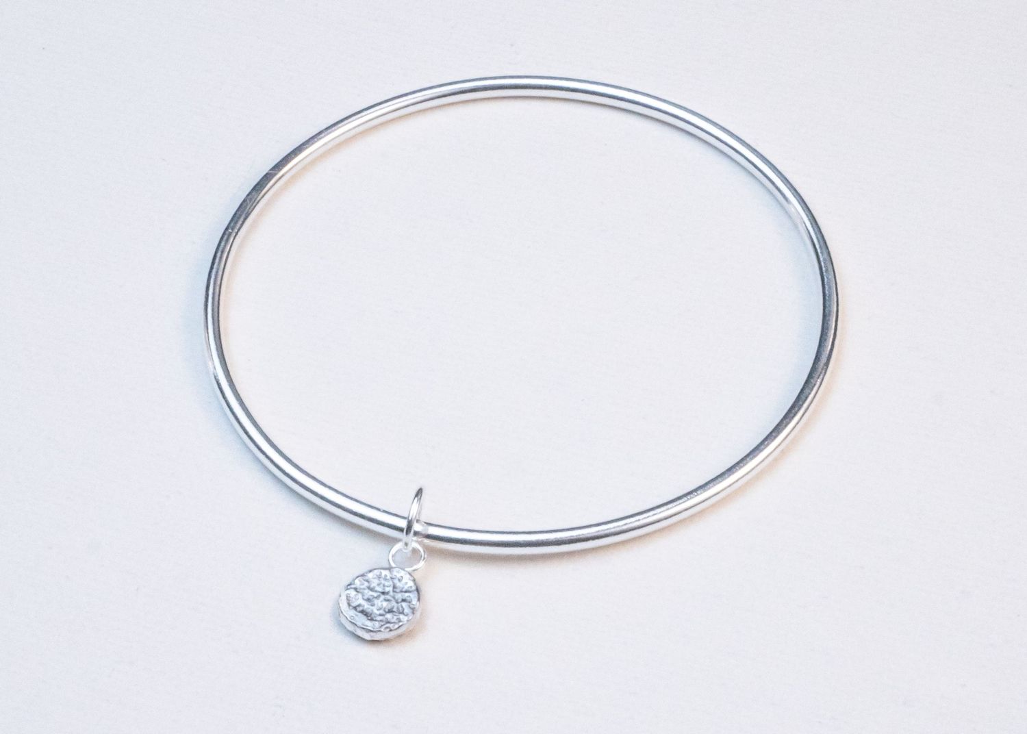 Four silver jewelry pieces including hoop earrings and a small charm displayed on a white background.