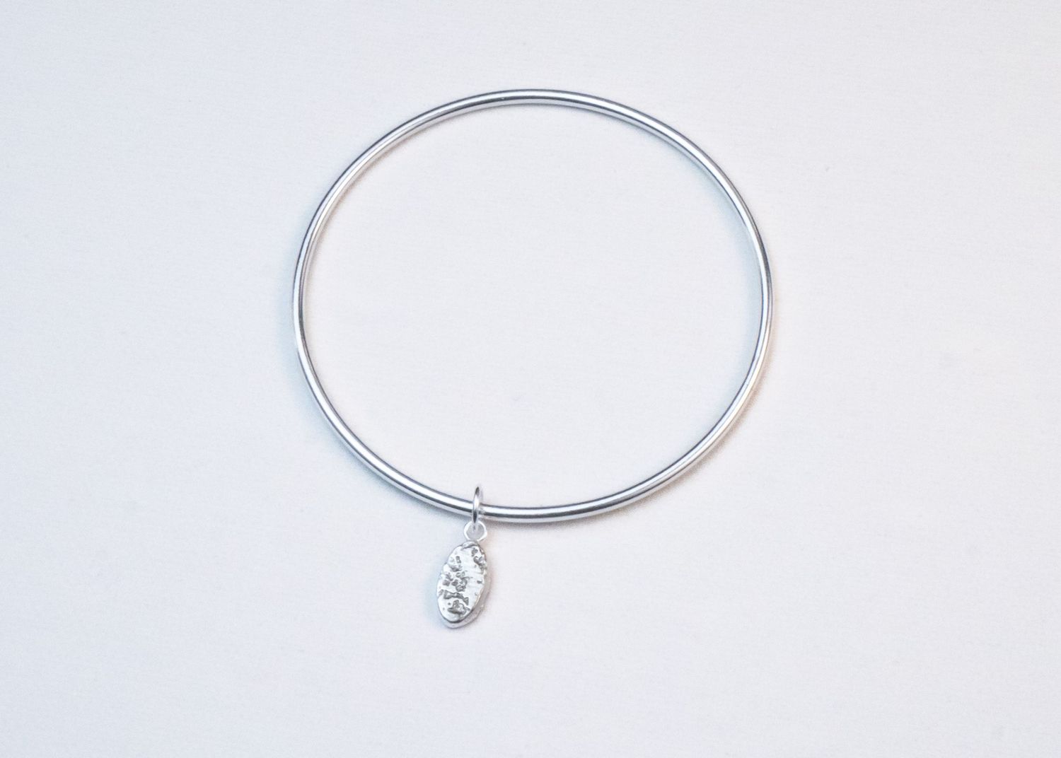 Minimalist silver bangle bracelet shown from multiple angles with a small crystal accent detail.
