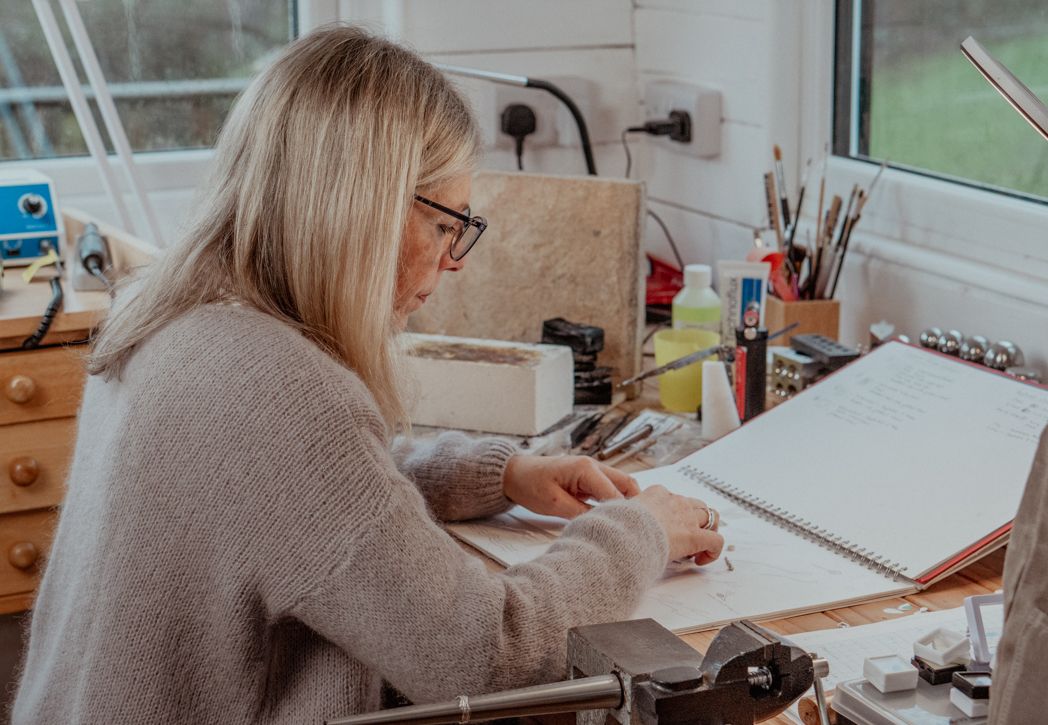 Artist sketching at a wooden desk by window with art supplies in cozy home studio workspace.