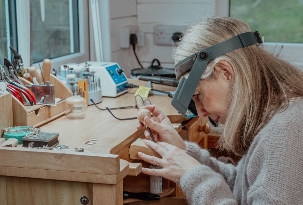 Focused artisan working at a well-equipped jewelry crafting workbench with tools and magnifying equipment.