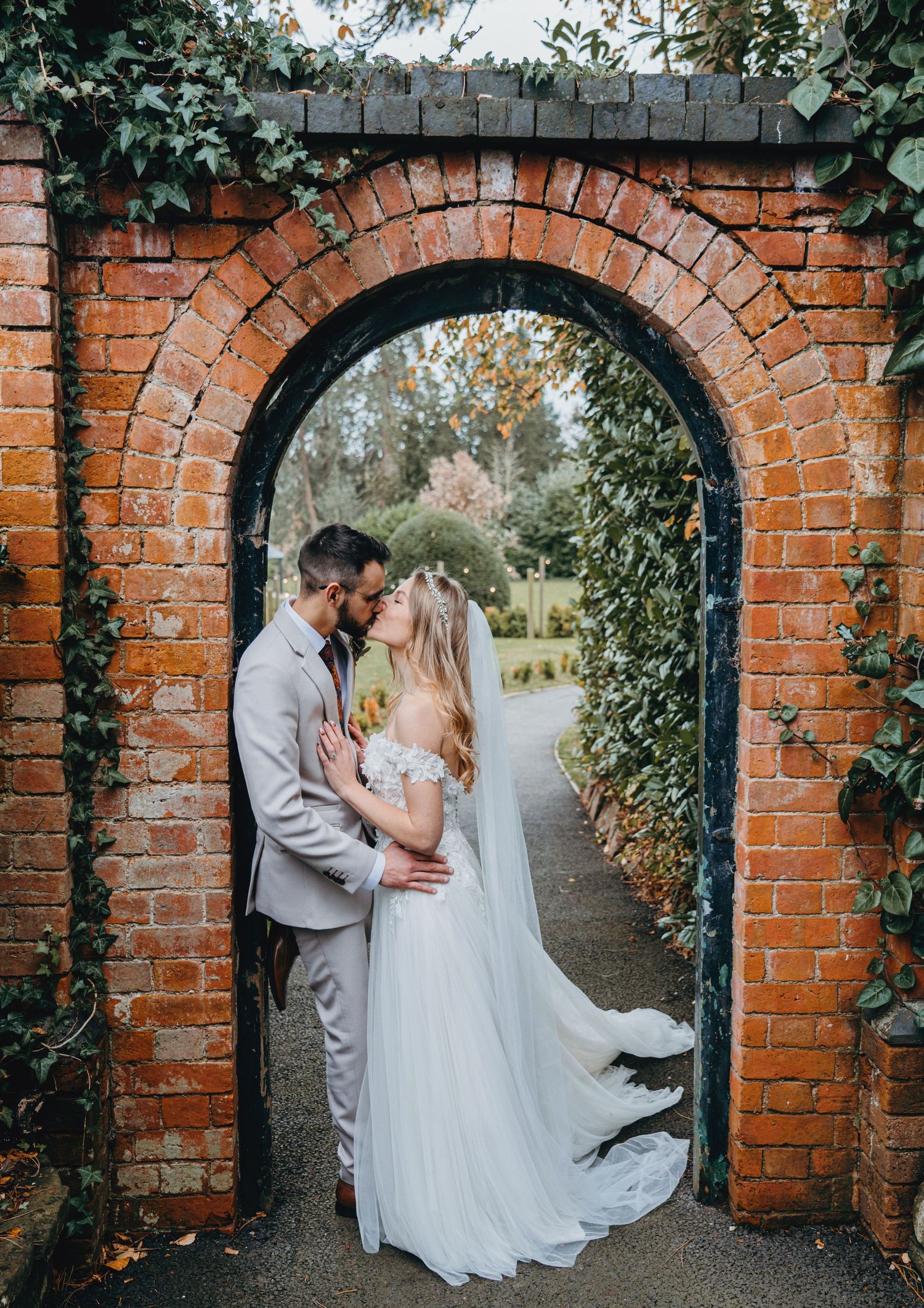 Newlyweds sharing an intimate moment under a rustic brick archway surrounded by greenery.