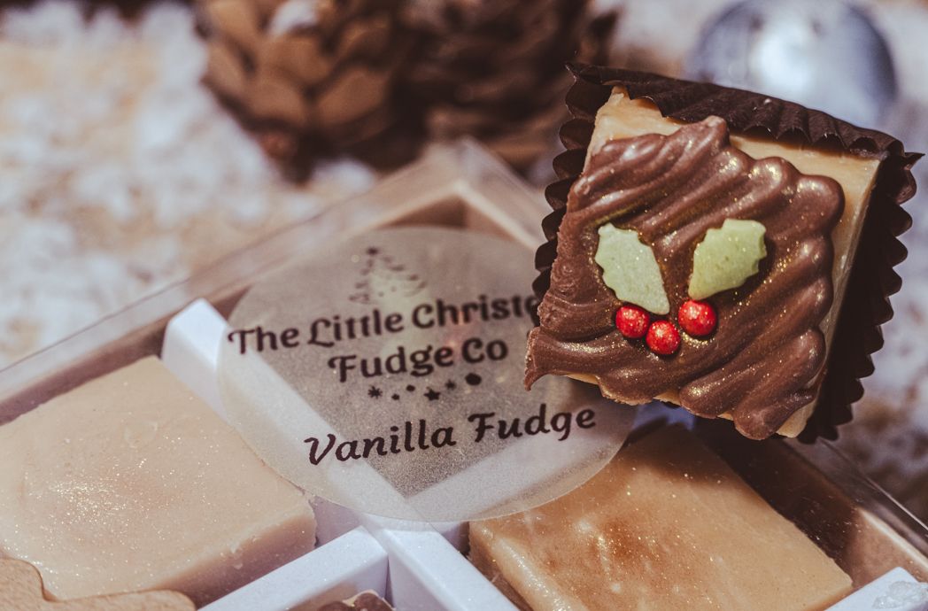 A piece of chocolate vanilla fudge decorated with holly leaves and berries sits on a Christmas-themed package.