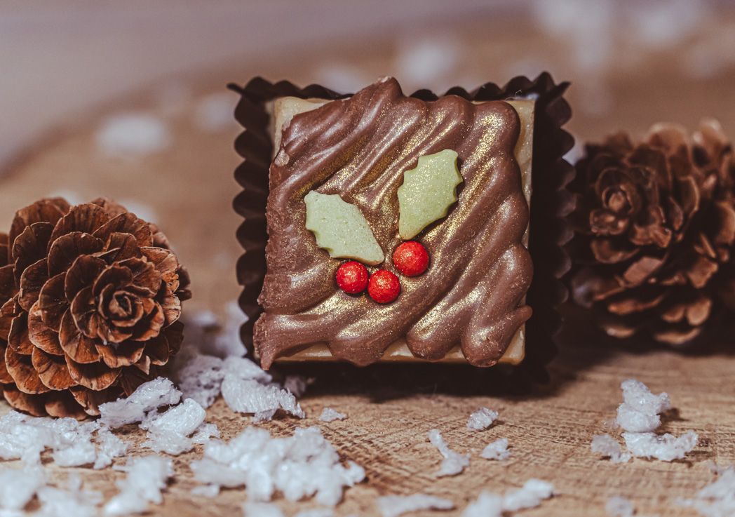 Festive chocolate brownie square decorated with holly leaf and berries design beside pinecones.