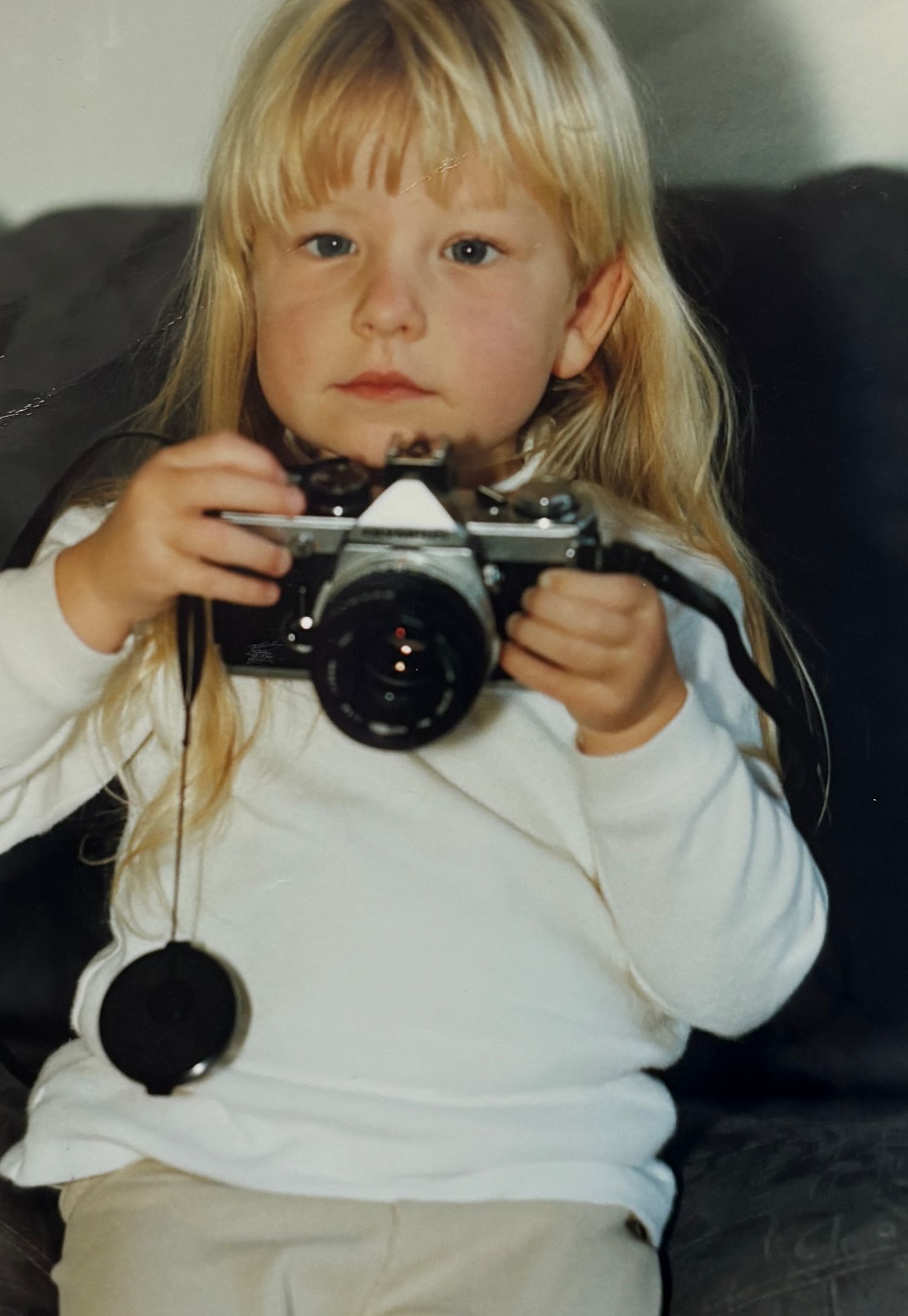 Young photographer holding a vintage camera while wearing a white sweater.
