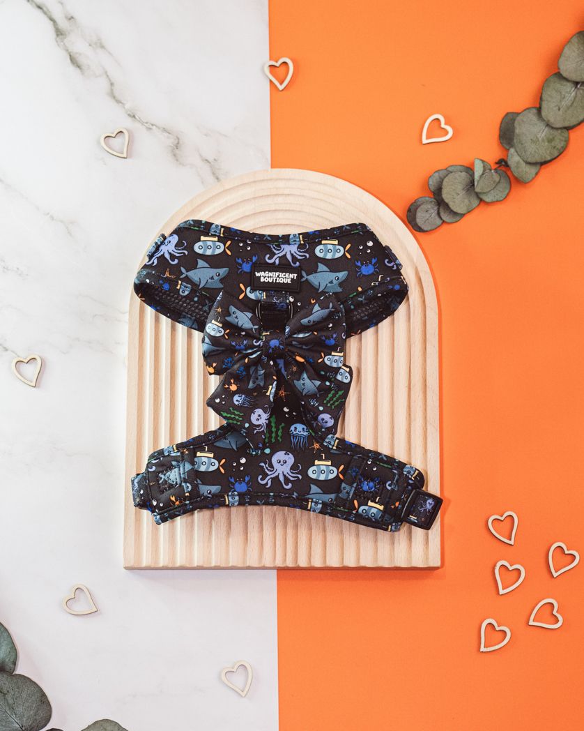 Navy blue dog harness with space-themed pattern displayed on beige and orange backdrop with heart decorations.