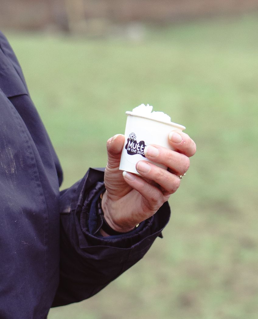 Hand holding a small white branded cup in outdoor setting.