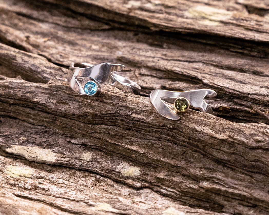 Two handcrafted rings with blue and green gemstones displayed on weathered wood.