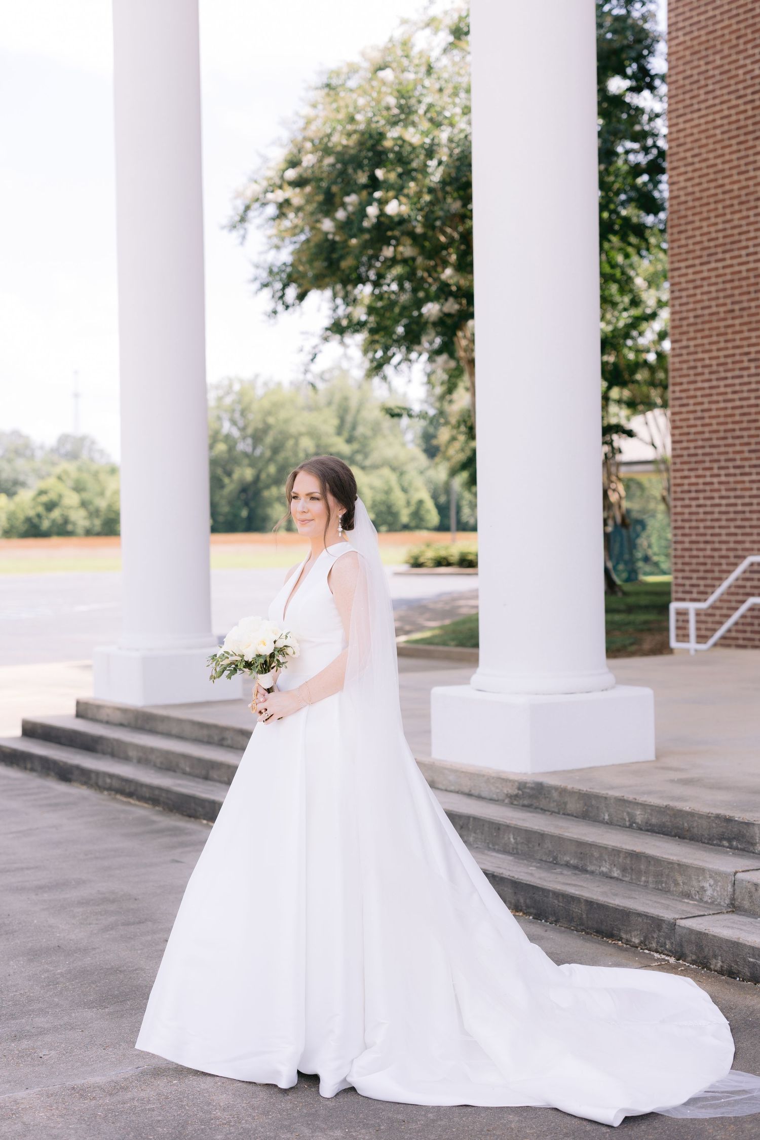 Classic bridal portrait under white columns with dramatic train spread across stone steps.