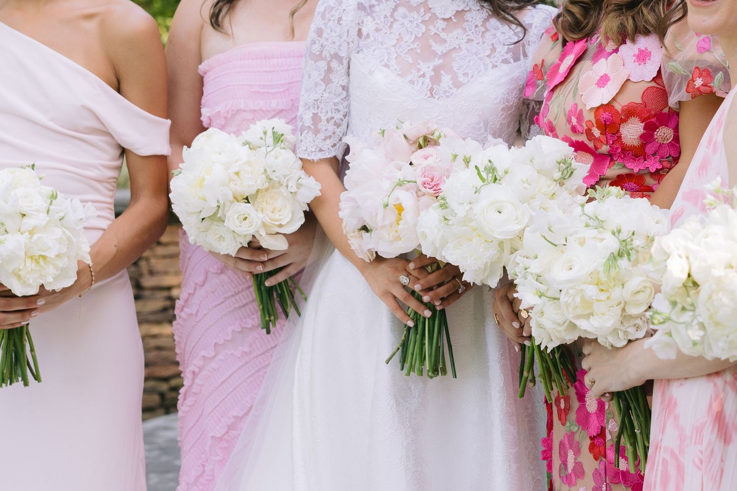 Bridesmaids in pink dresses hold fresh white and pink floral bouquets at an outdoor wedding ceremony.