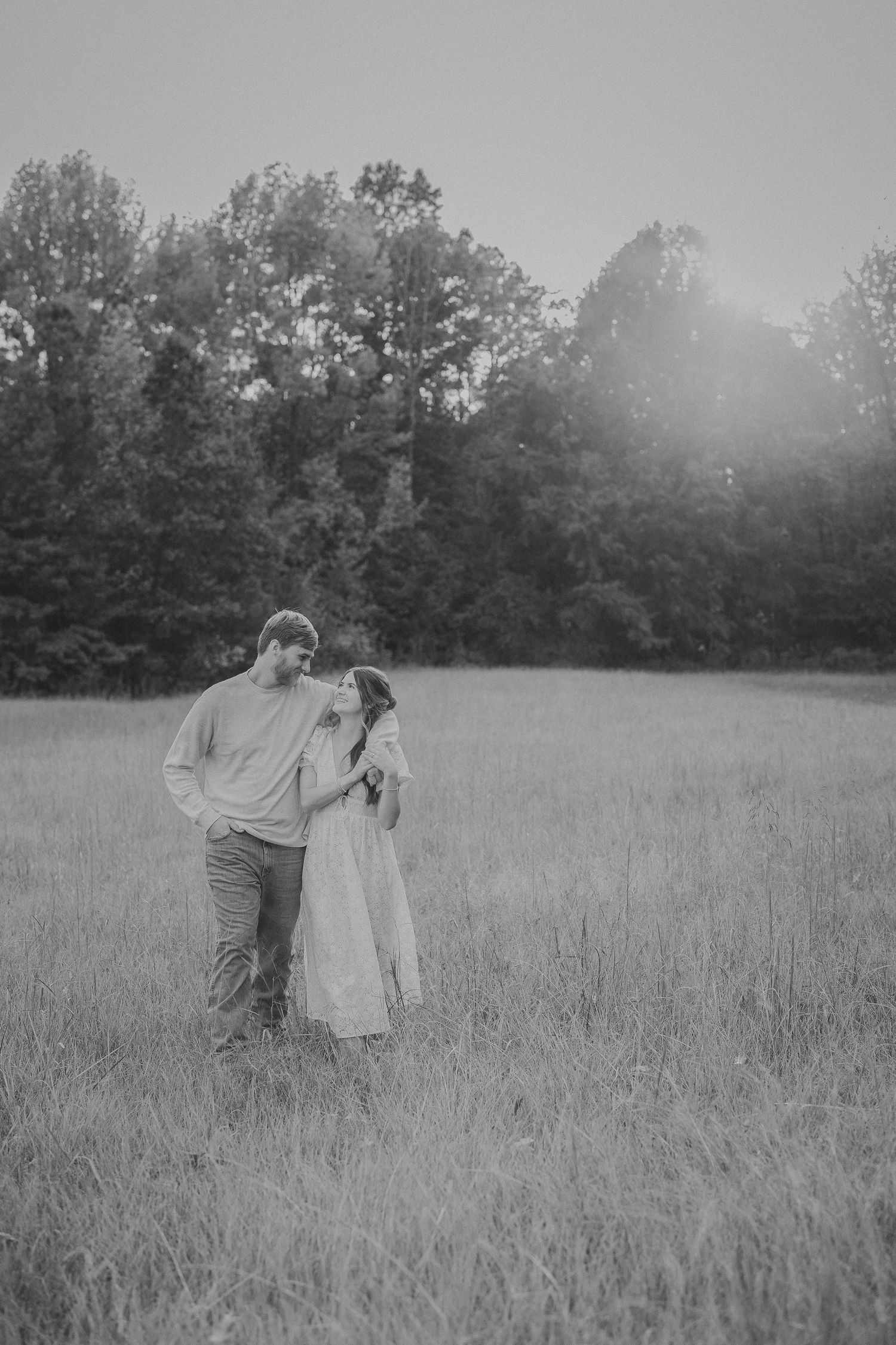 Two figures embrace tenderly in a misty meadow during a romantic black and white photoshoot.