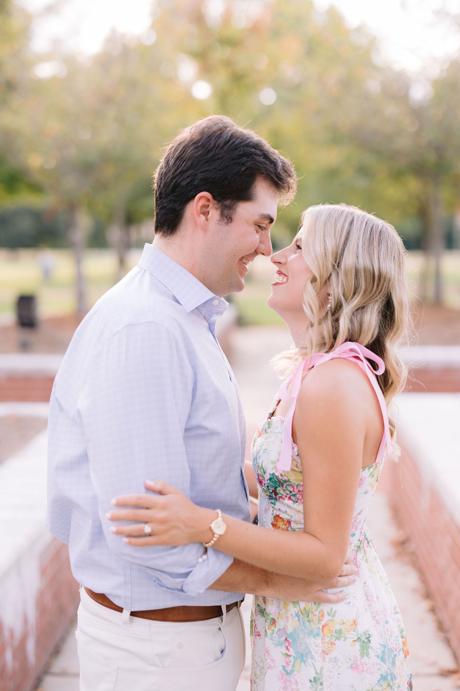 A romantic couple shares tender moments in a park setting wearing light spring attire and embracing.