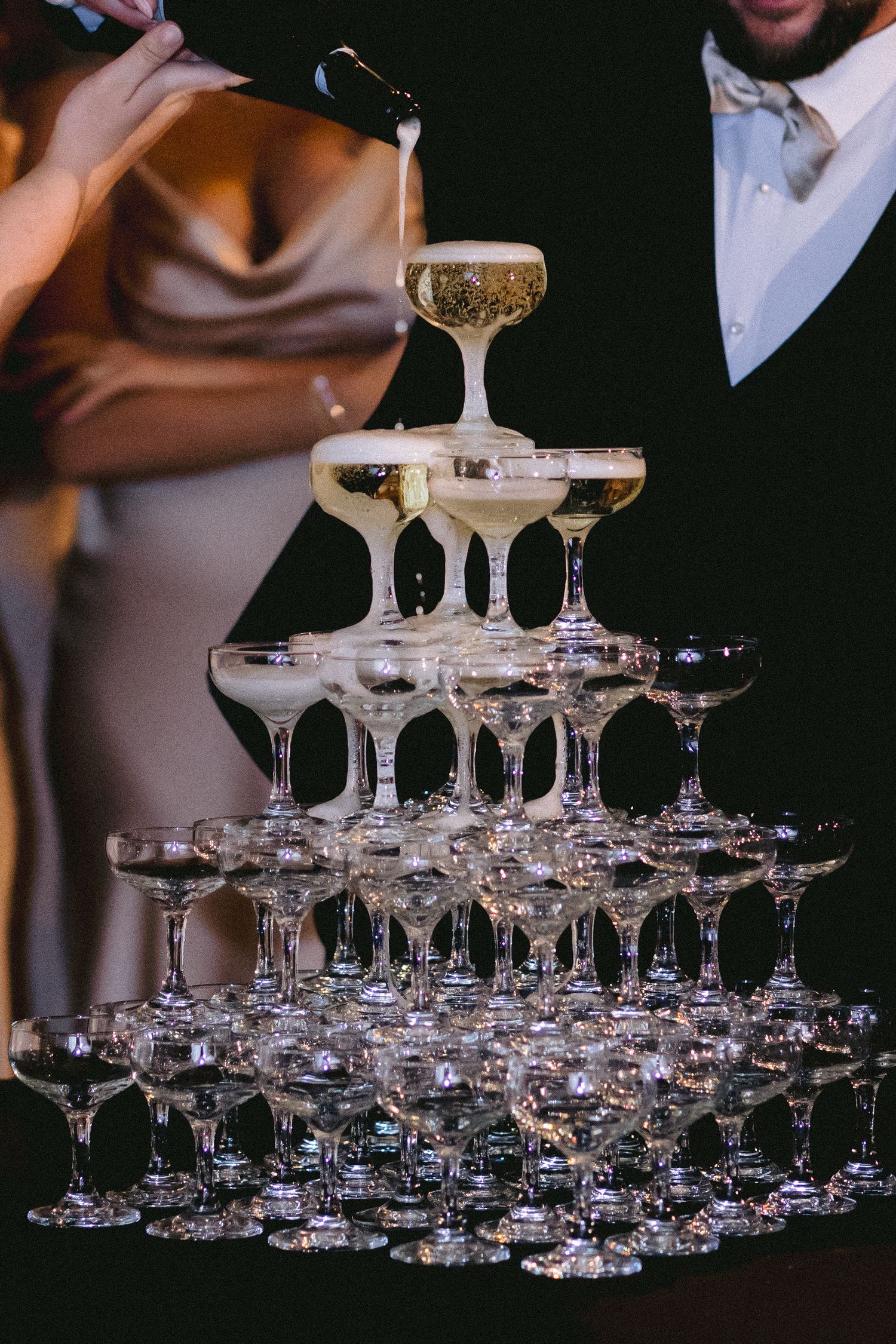 Elegant champagne tower with crystal coupe glasses stacked in multiple tiers being filled with sparkling wine.