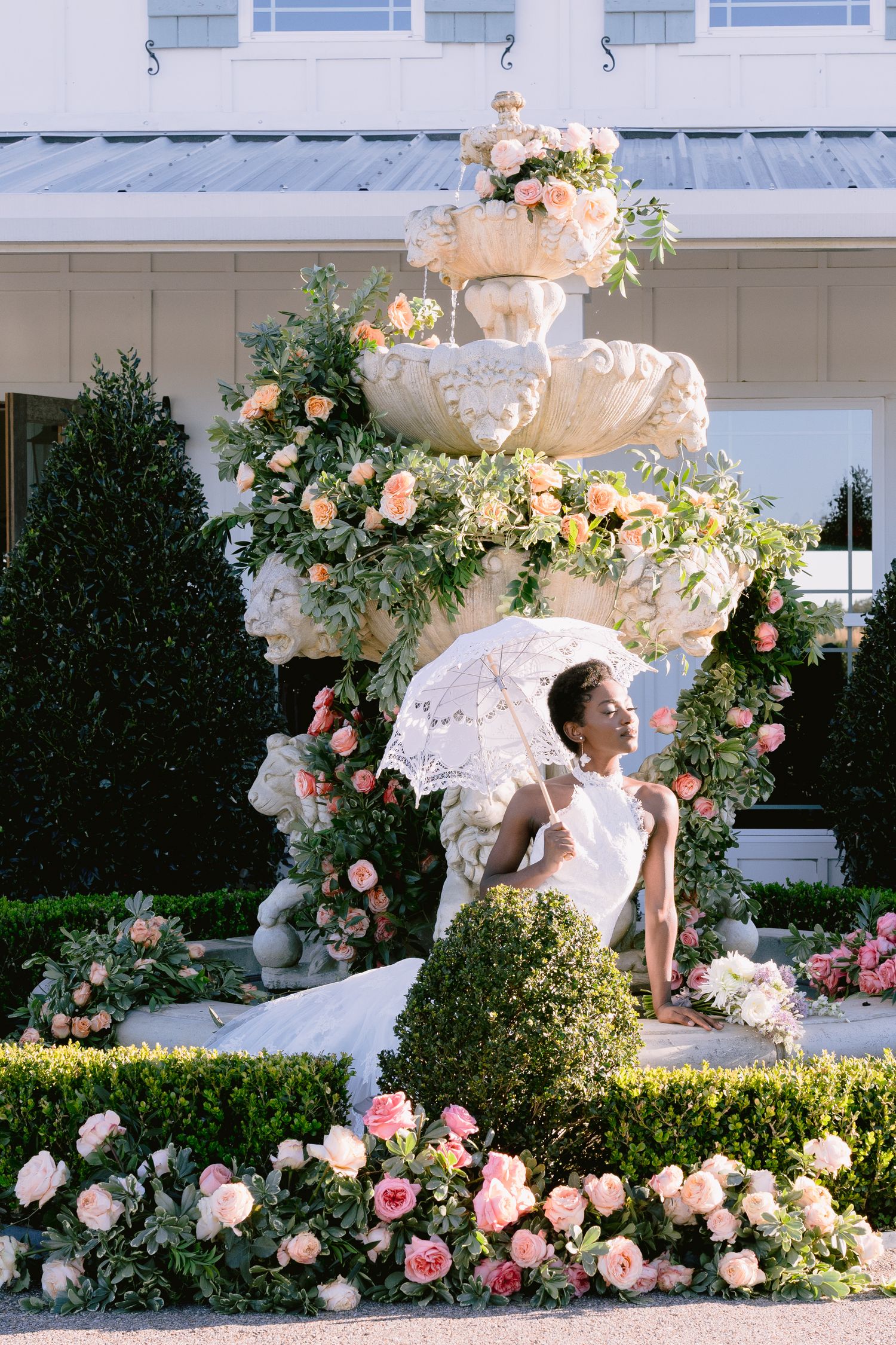 Romantic garden setting with ornate stone fountain surrounded by pink roses and wedding dress details.