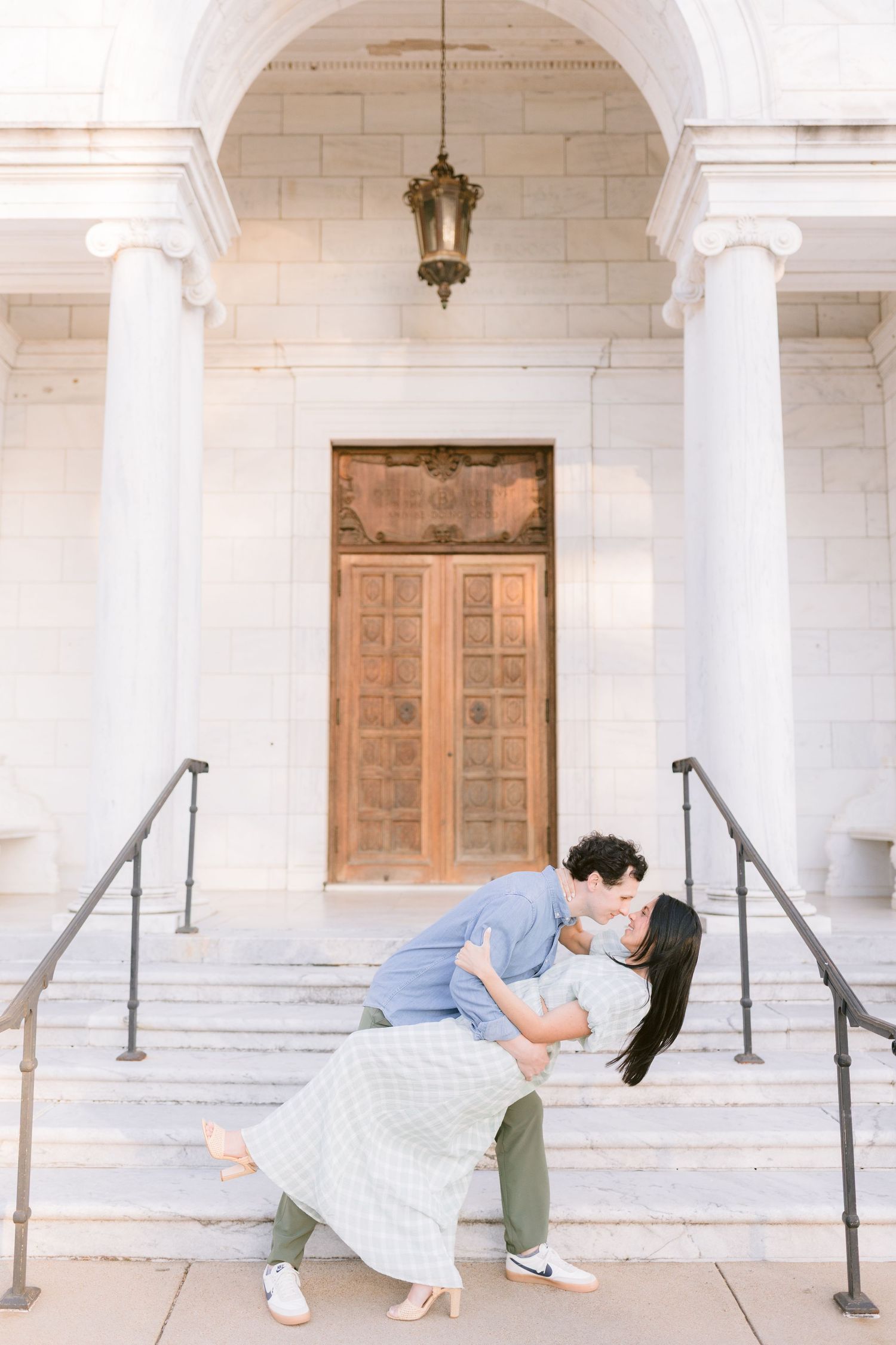 A romantic couple pose for engagement photos under white stone archways and columns at sunset.