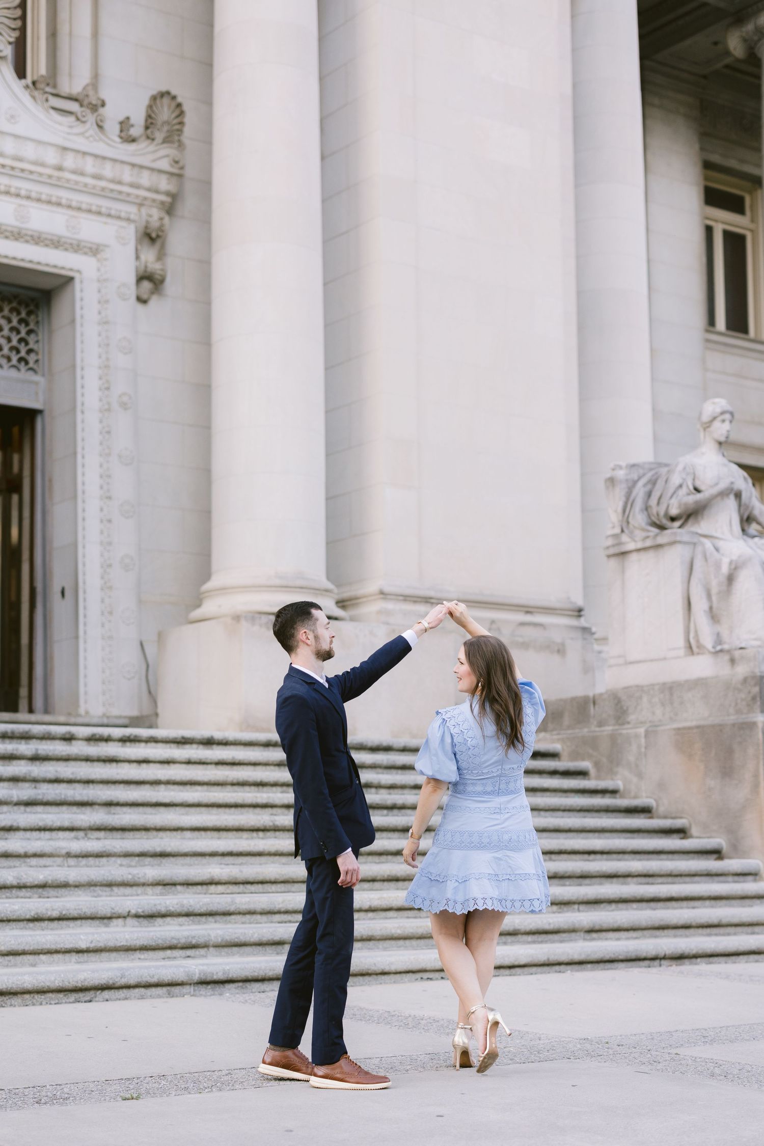 A couple dancing together in front of a grand columned building entrance with white stone steps.