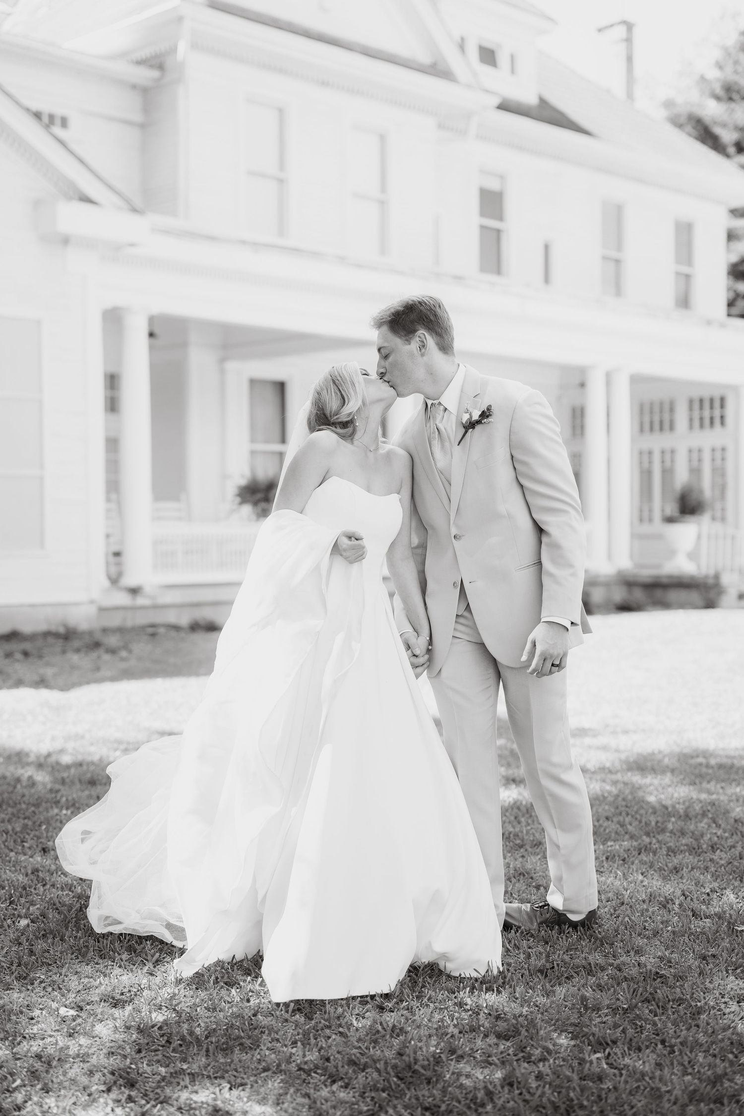 Black and white wedding portraits showing a couple embracing on the lawn of a white building.