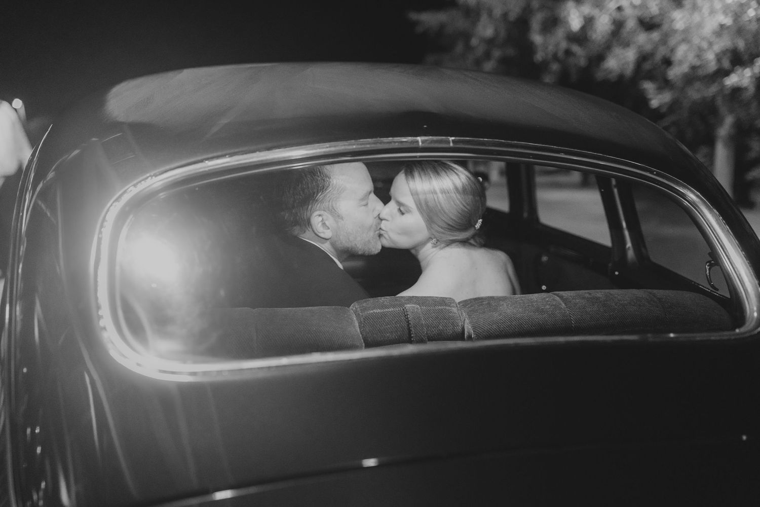Classic black car transporting newlyweds in dramatic nighttime shot.