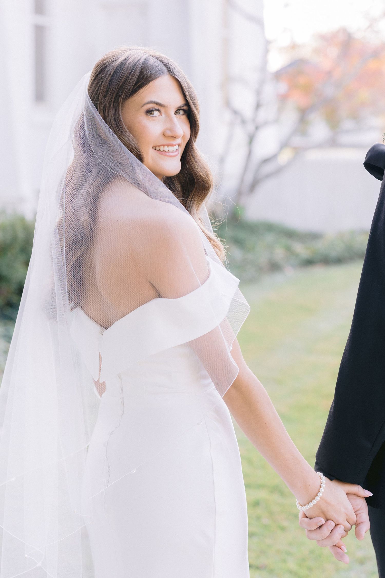 Ethereal bride in a flowing white dress and veil smiles during an outdoor wedding photoshoot.