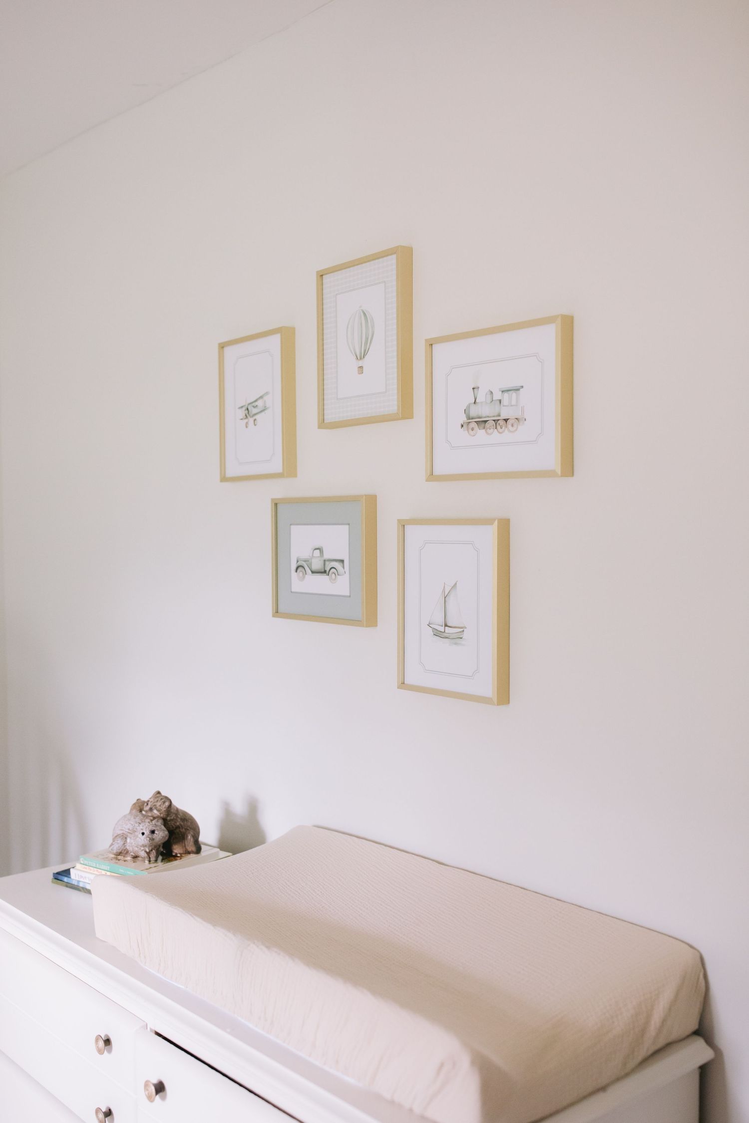 Minimalist nursery changing table with beige cushion pad and framed artwork gallery wall in light wood frames.