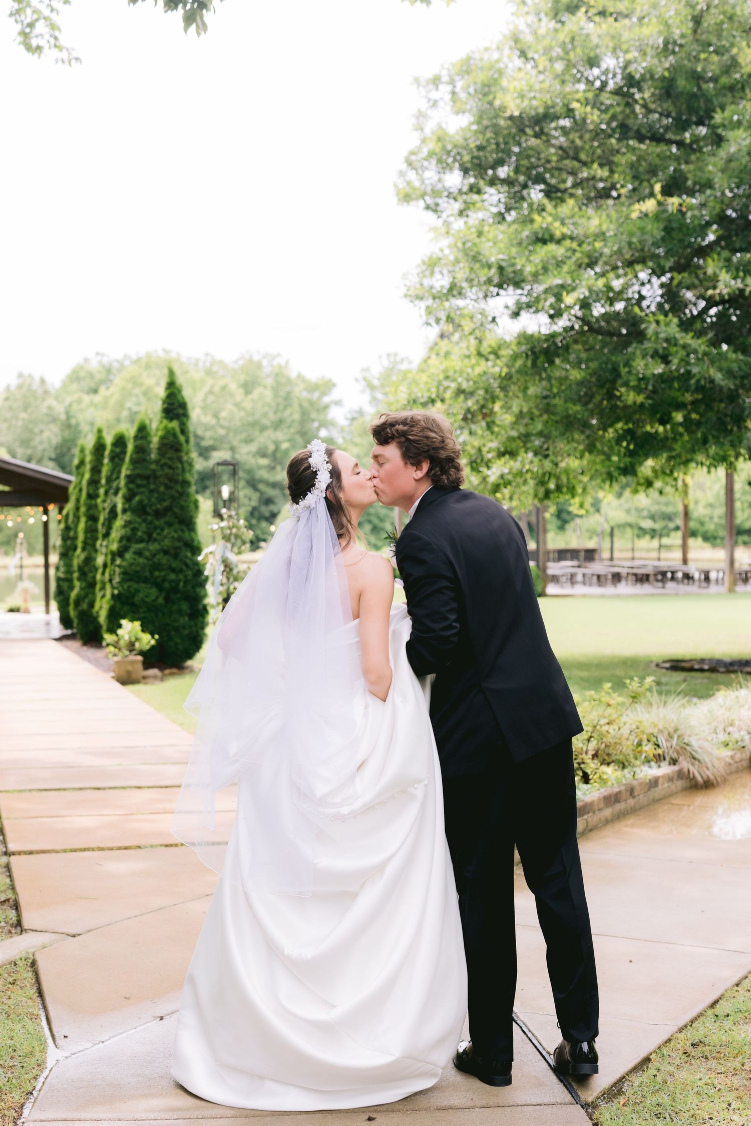 Newlyweds walking along garden path with flowing white wedding dress train.