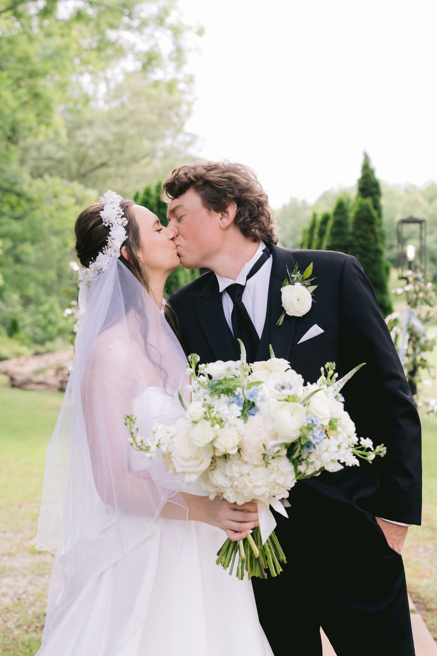 Romantic wedding couple sharing a kiss while holding white floral bouquet in garden setting.