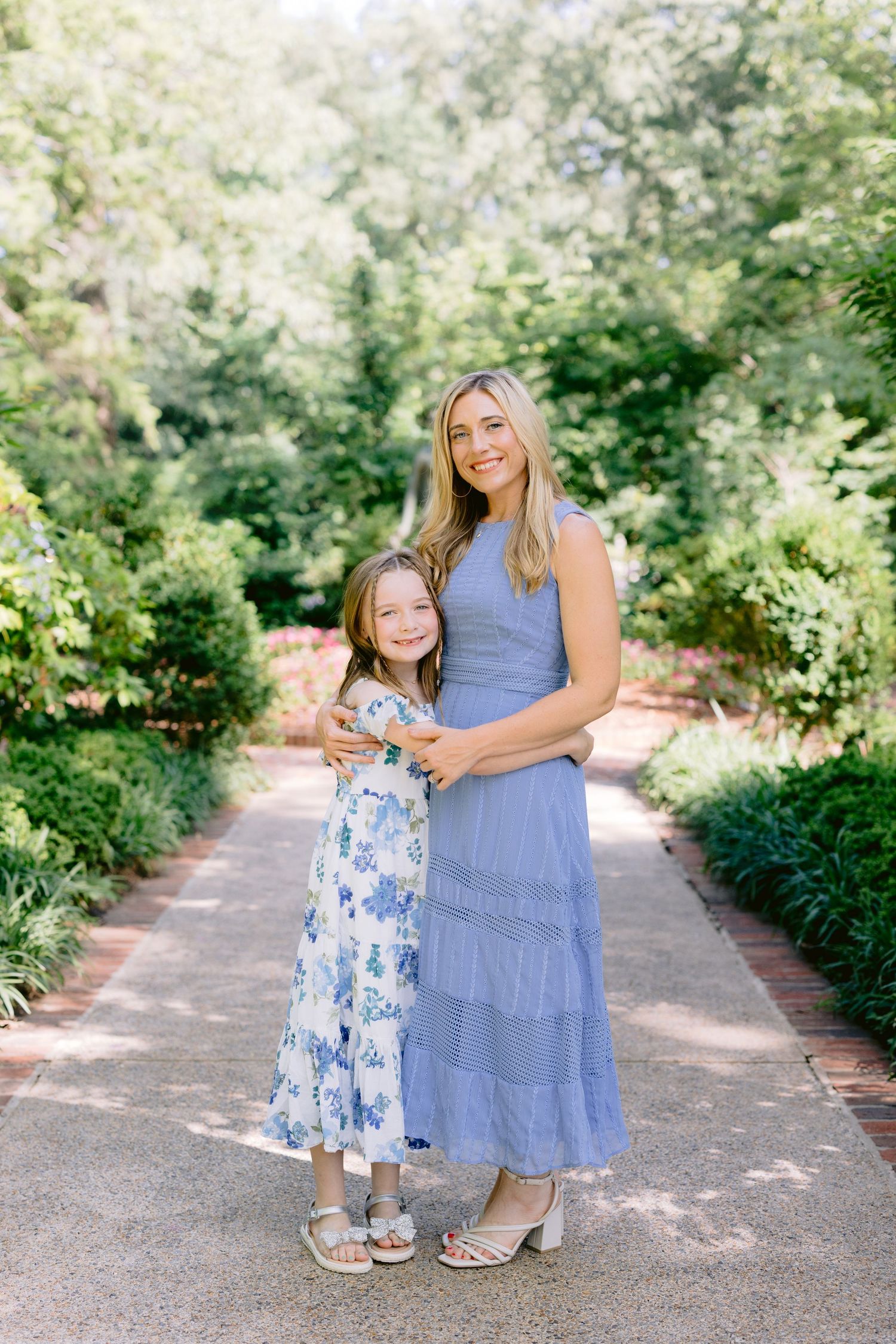 Family portrait on garden pathway with blue and floral summer dresses in outdoor nature setting.
