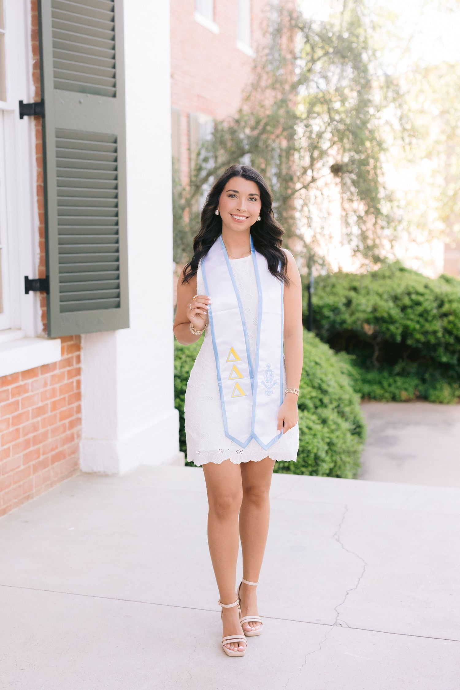 A bright and elegant springtime outfit with white shorts and a light blue blazer worn against a brick exterior.