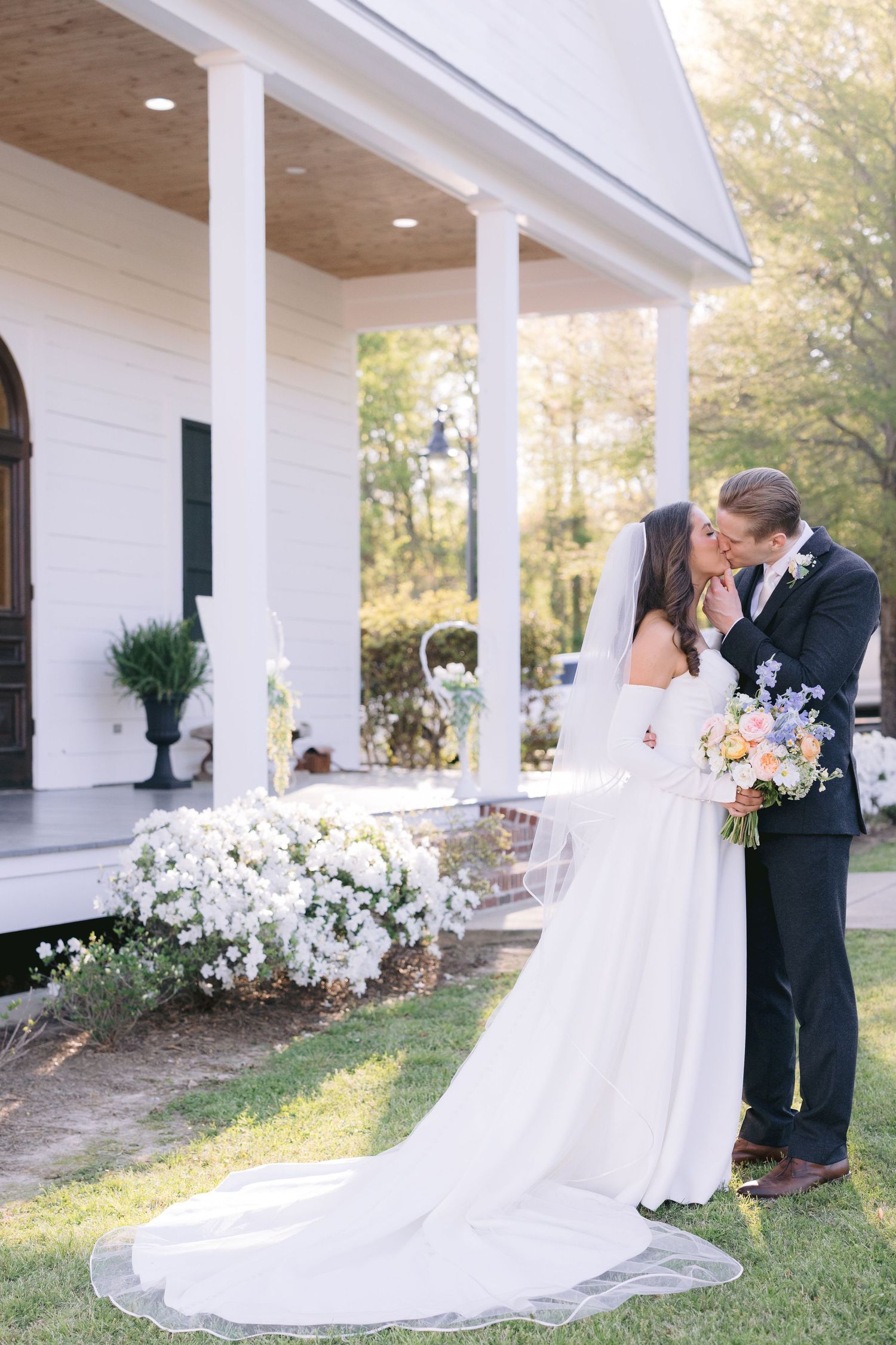 Wedding couple shares romantic moments under a white columned porch of a Southern style chapel, the mill at plein air in Taylor, MS.