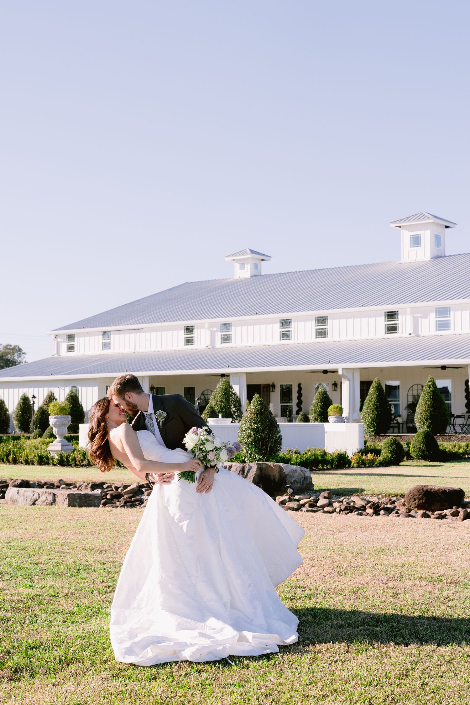 Ethereal bridal portraits on sprawling lawn with white farmhouse building in background.