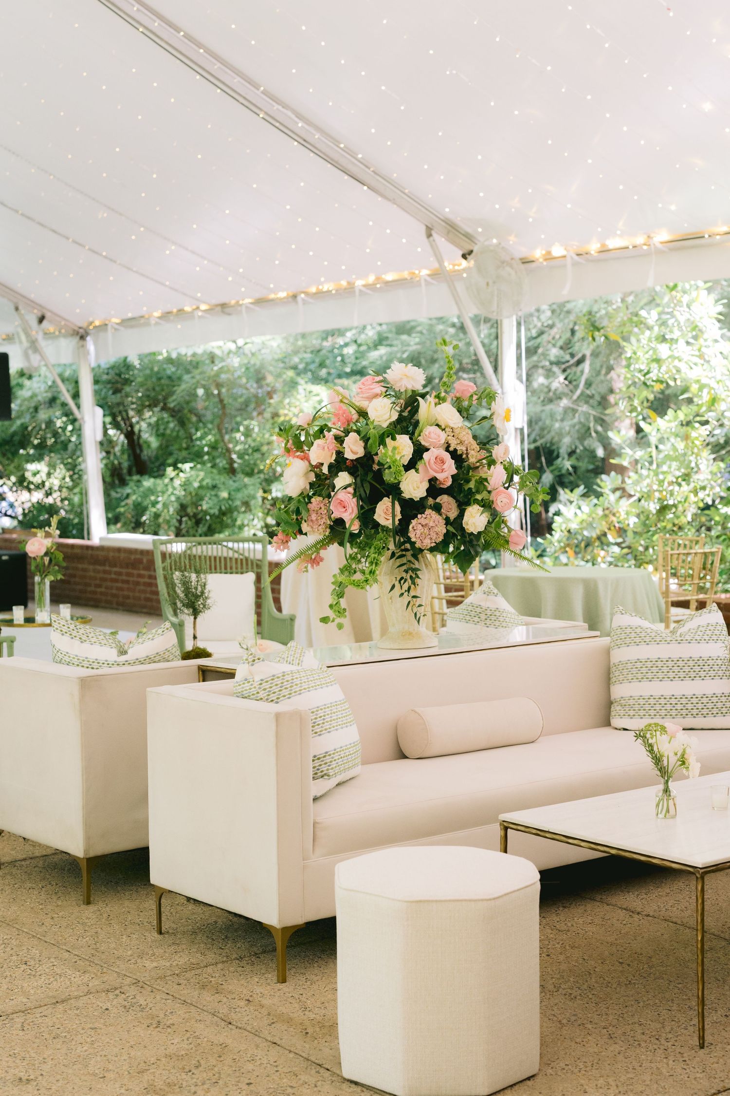 Elegant white lounge furniture with peach floral arrangements set up for an outdoor event under a white tent.