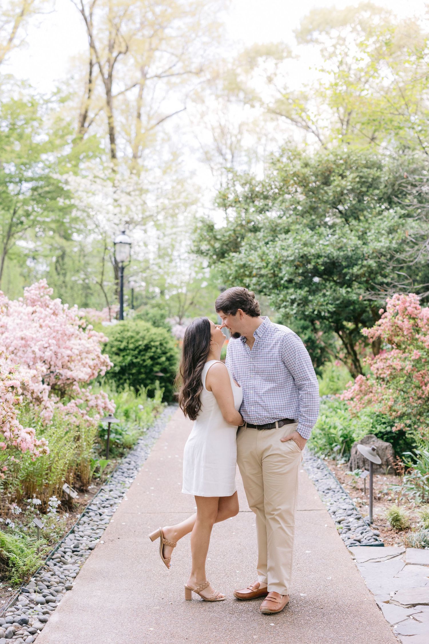 A romantic sequence of a couple walking and sharing a tender moment along a garden path with pink flowers blooming.