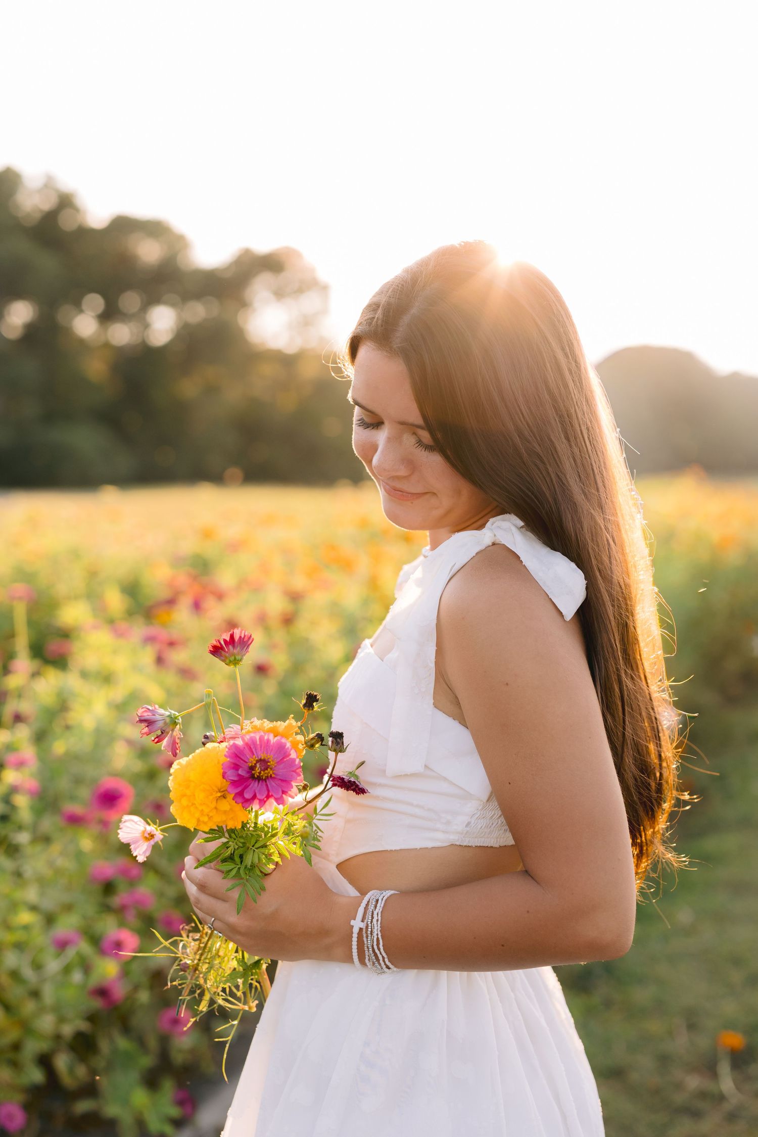 A person in a white dress stands in a vibrant flower field at golden hour while holding fresh-picked blooms.