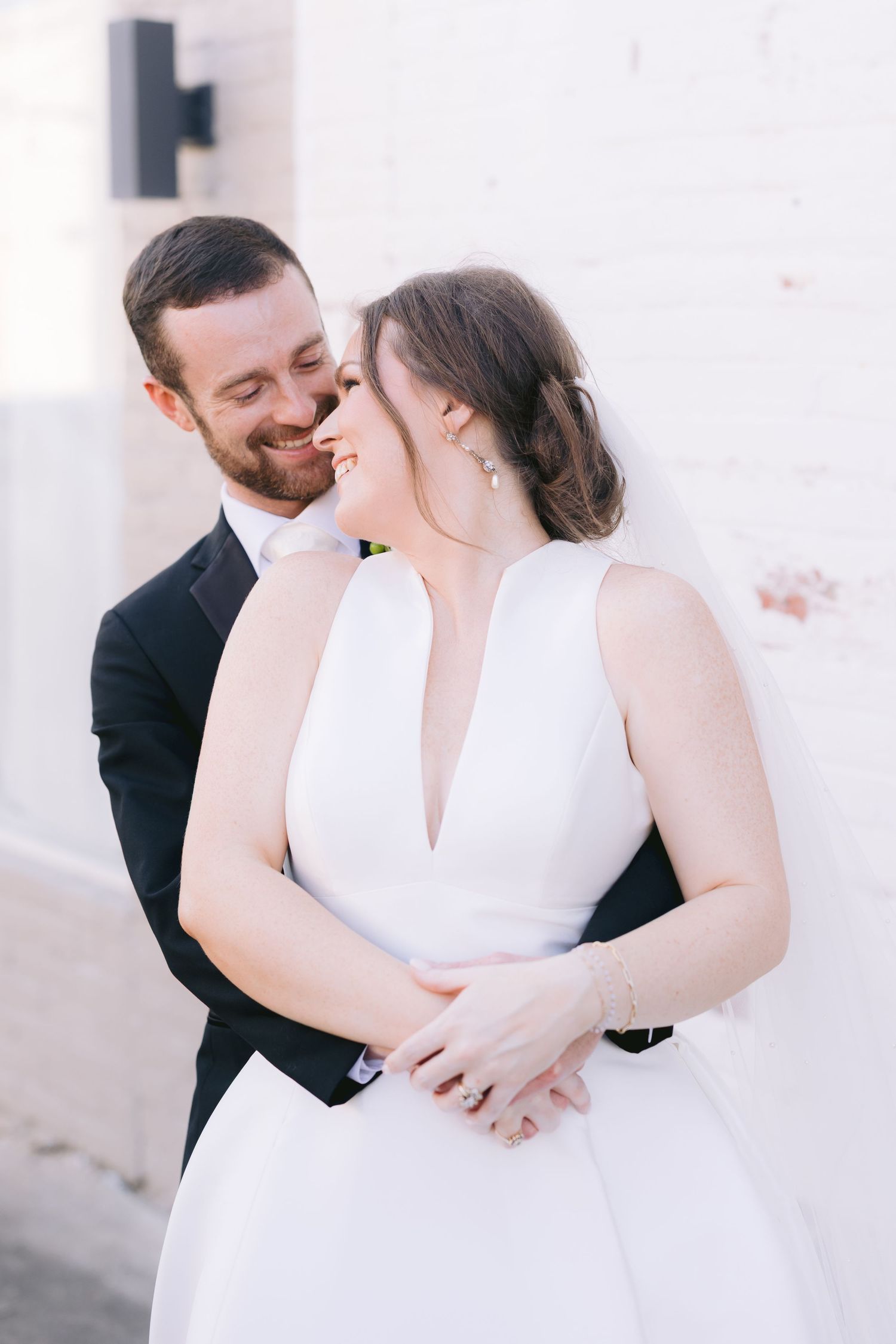 Joyful wedding couple sharing intimate moment against white wall.