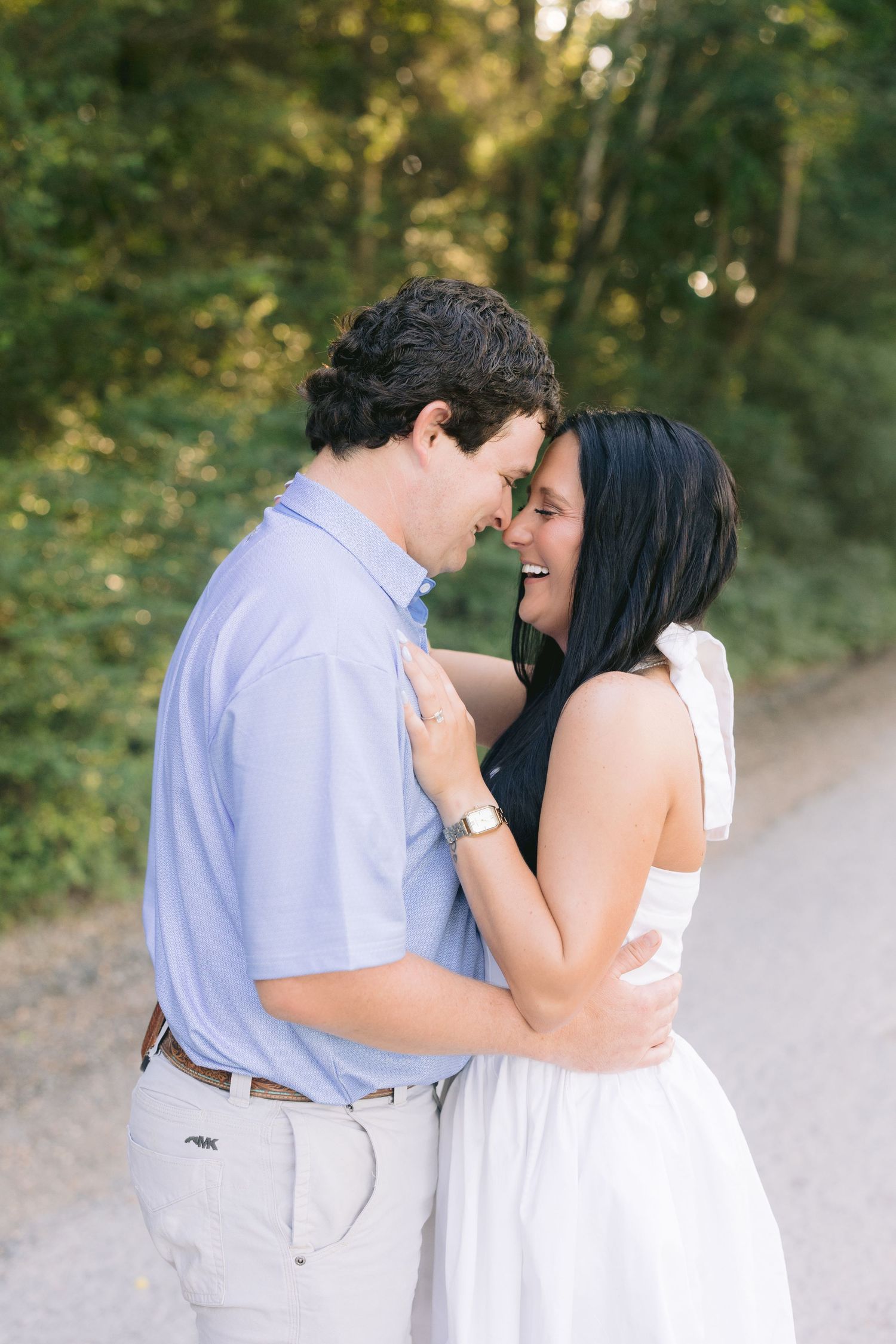 A romantic outdoor portrait of a couple sharing an intimate moment on a wooded path in soft lighting.
