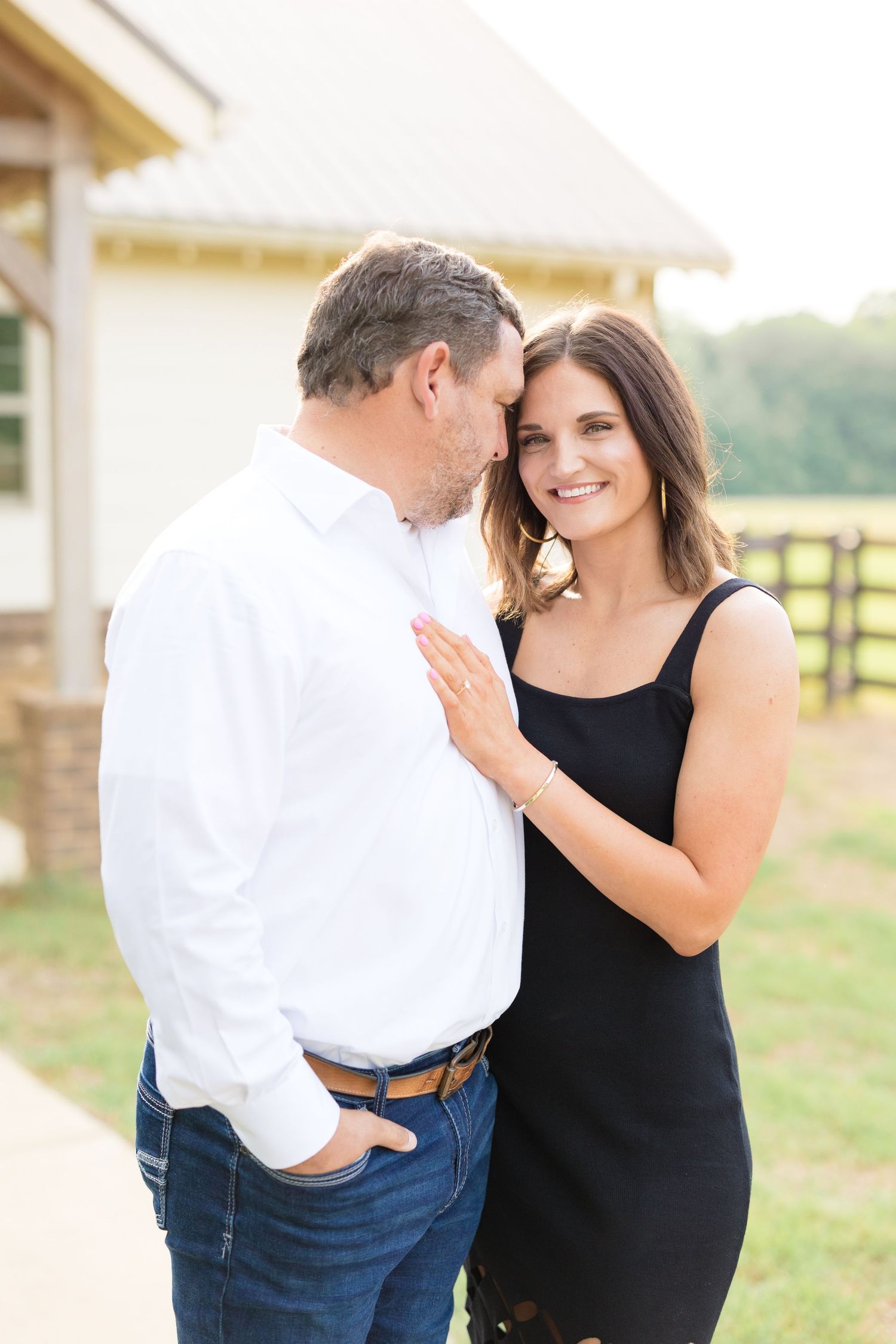A couple in black and white outfits share intimate moments outdoors during a photo session against a scenic backdrop.