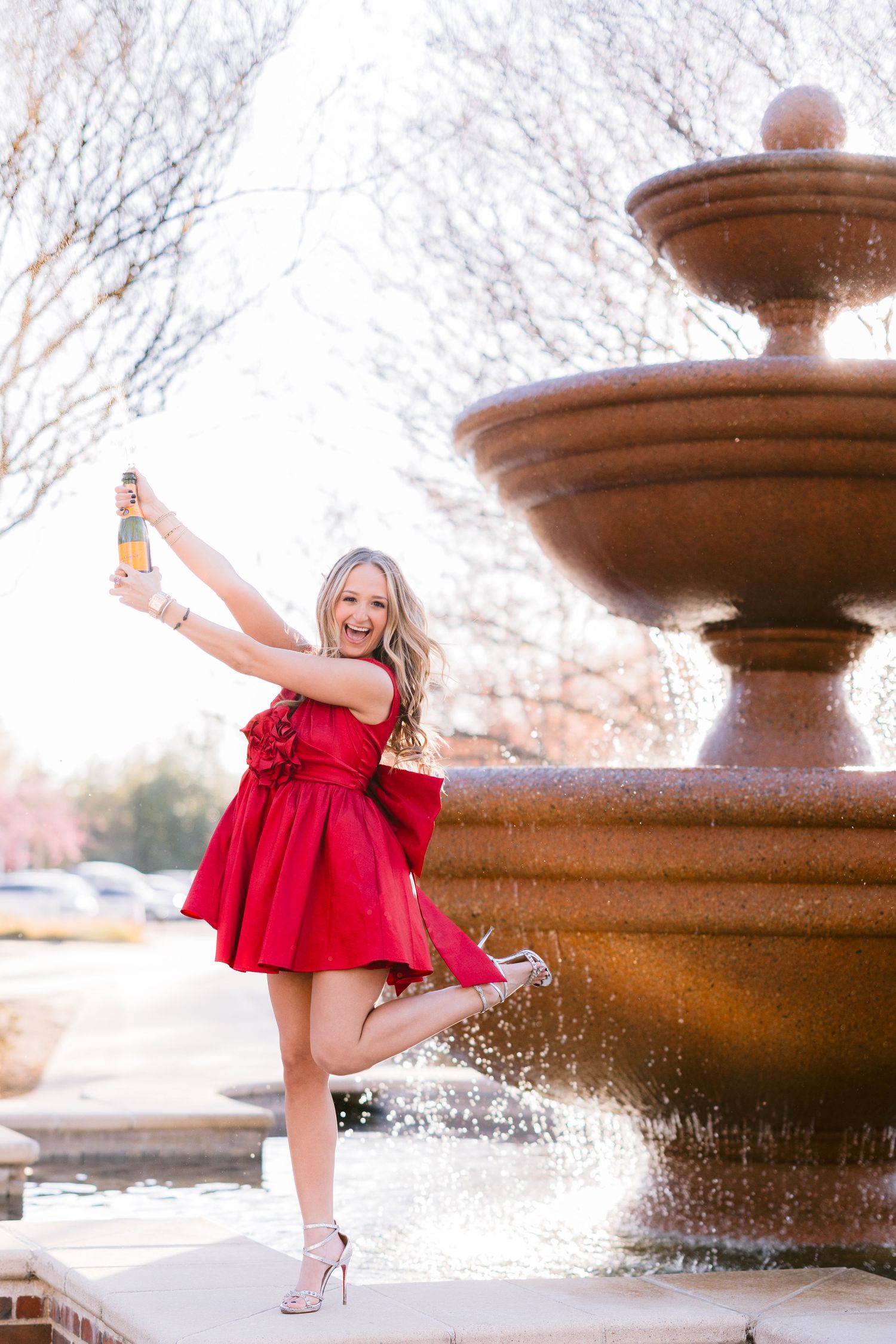 A red dress twirls gracefully near a fountain, creating a dynamic motion effect against a winter landscape.