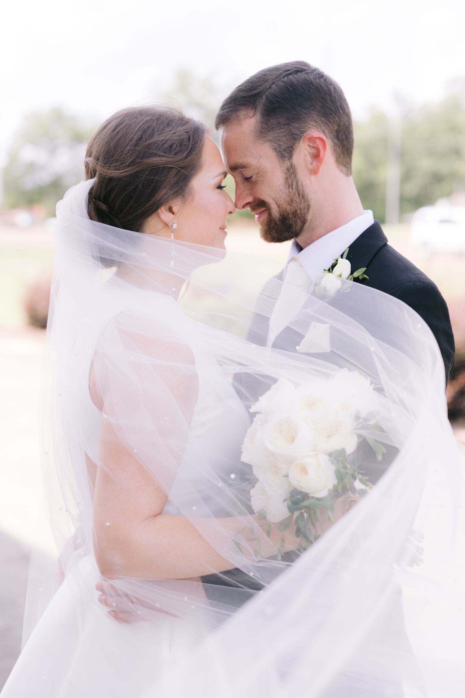 Tender moment between couple wrapped in flowing white veil.