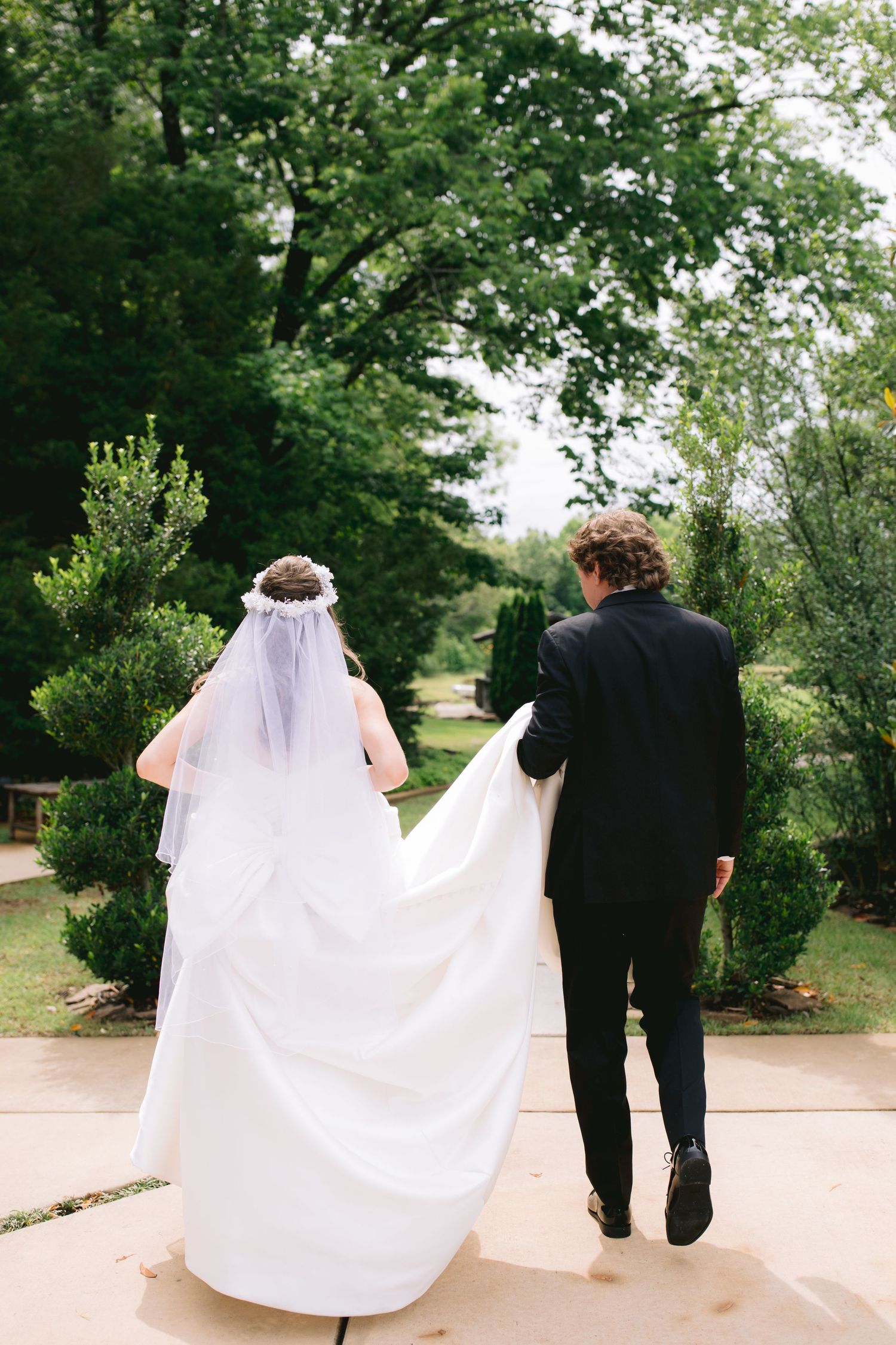 Wedding couple walking together on garden path with bride's dress trailing behind.