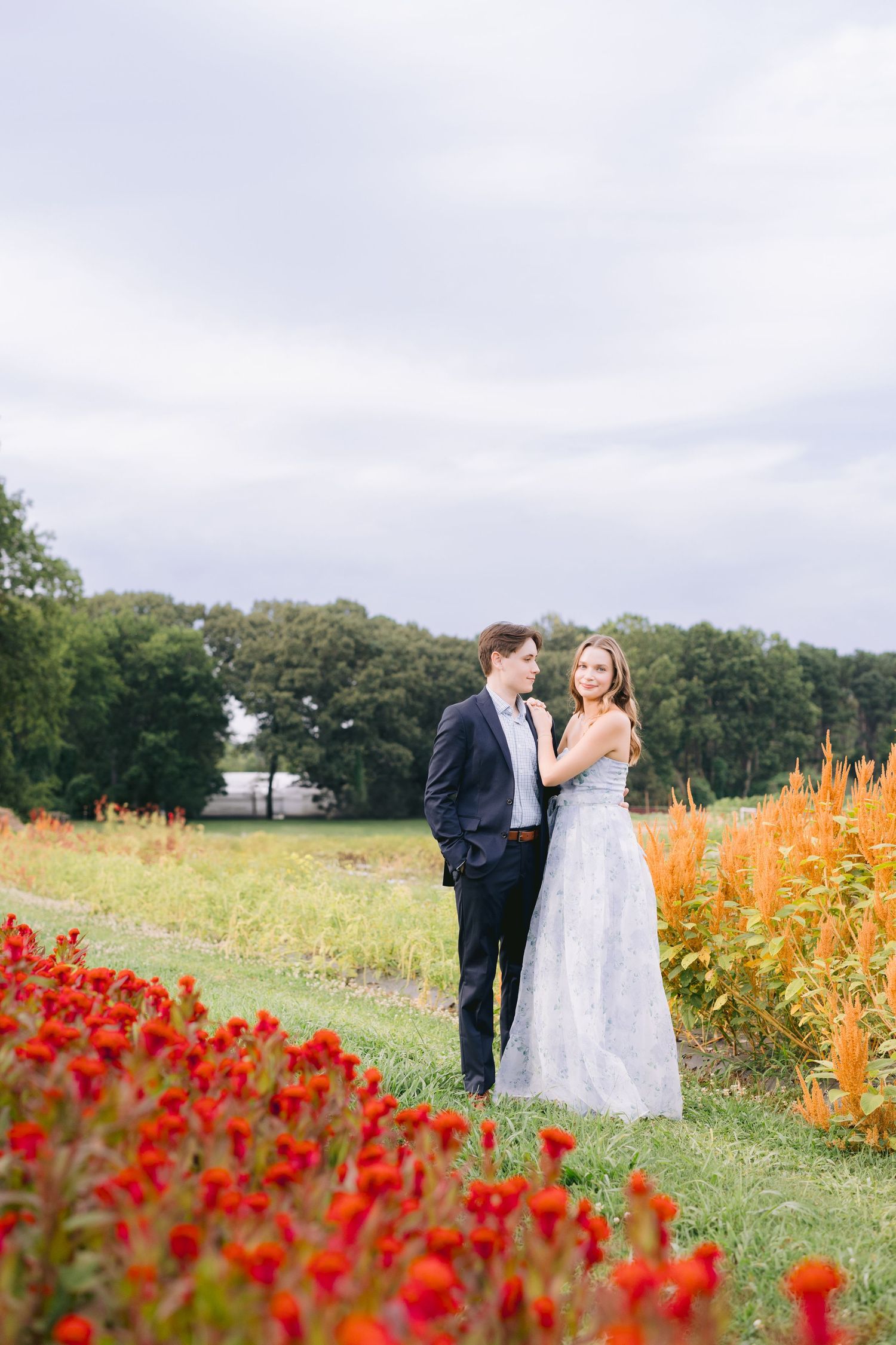 Couple shares romantic moment in a field of vibrant red tulips and orange flowers on a cloudy day.