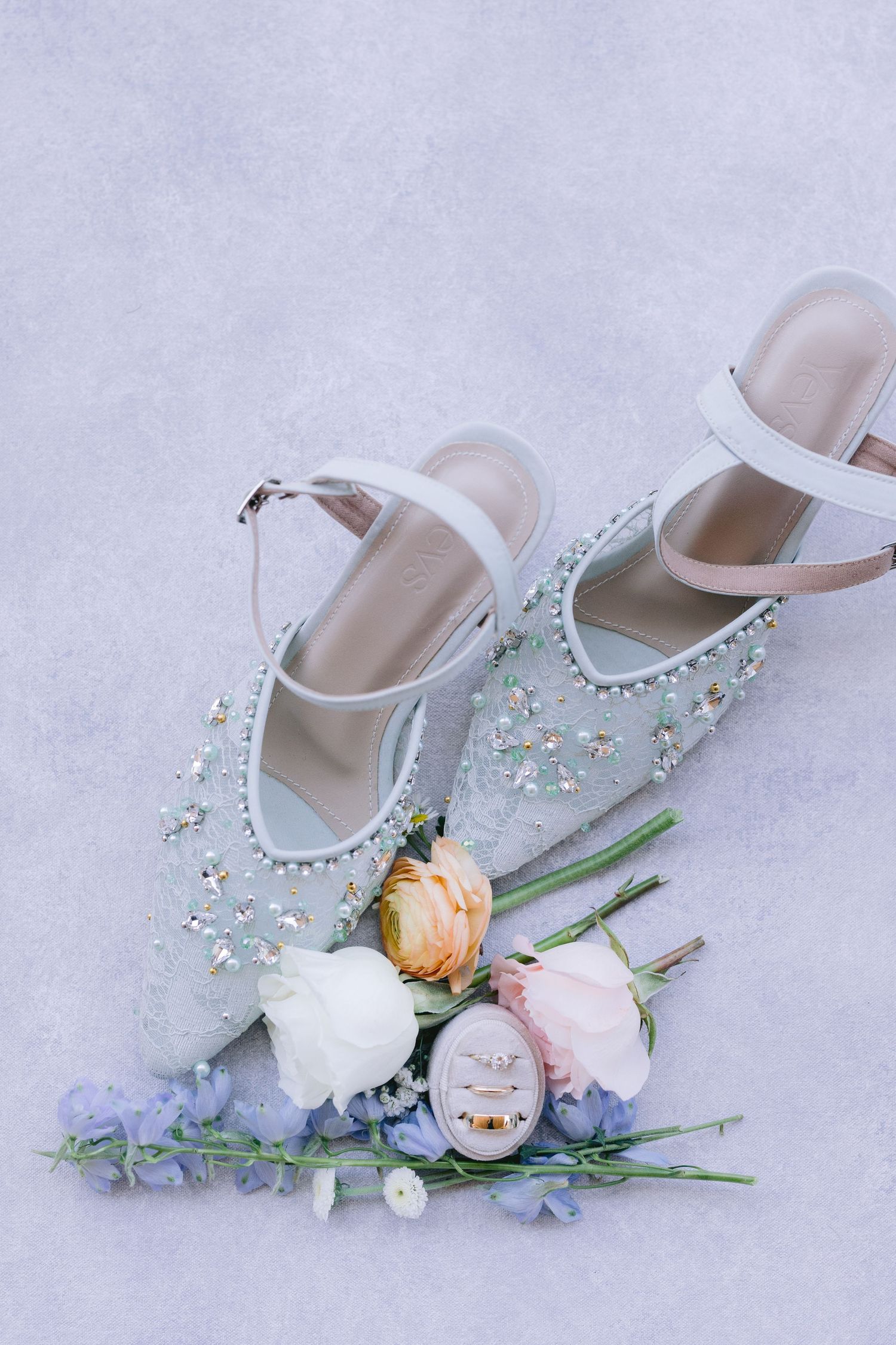 Delicate white bridal shoes decorated with crystals and pastel flowers against a light background.