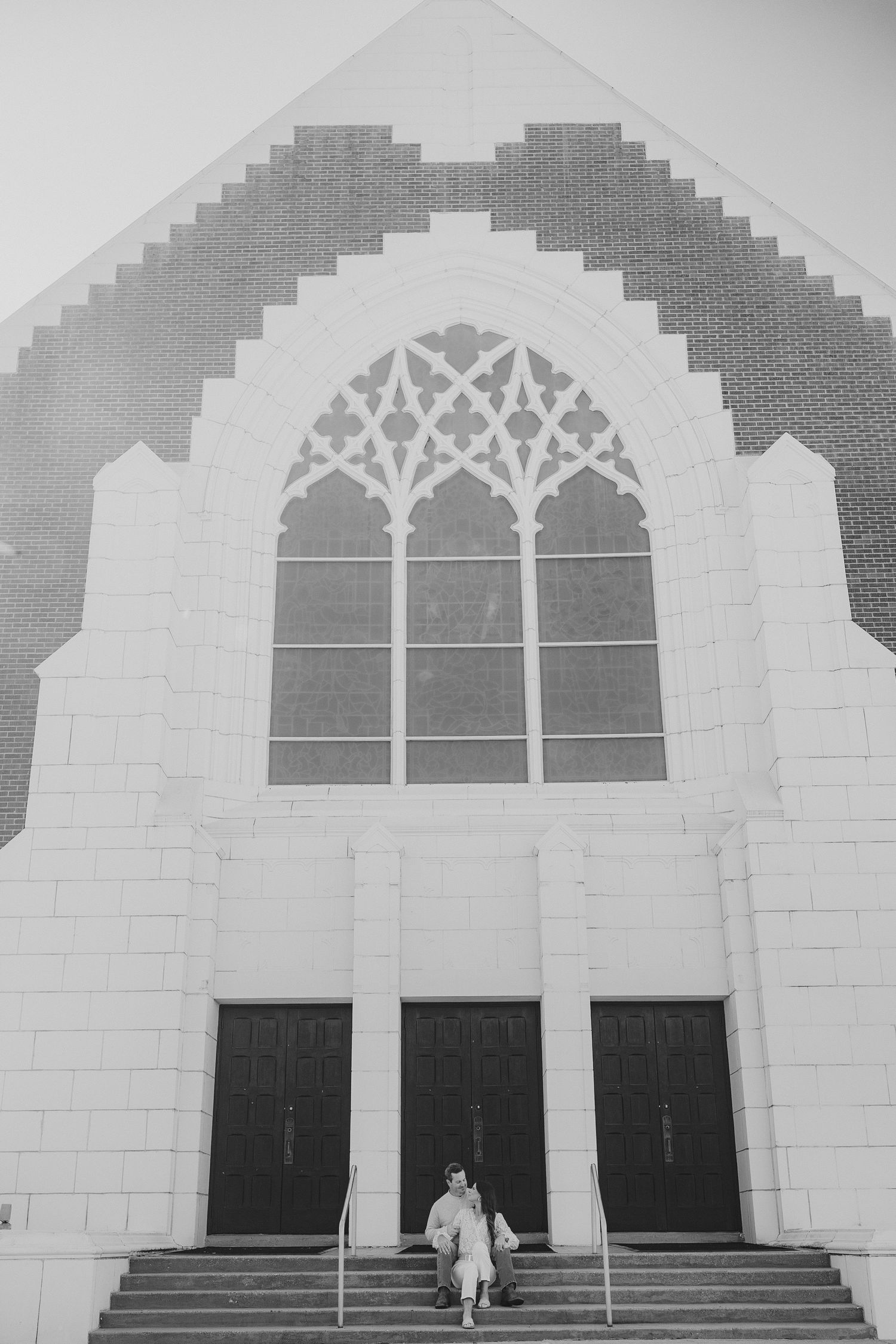 A classic church exterior with Gothic arched windows and three doors, featuring a minimalist black and white architectural composition.